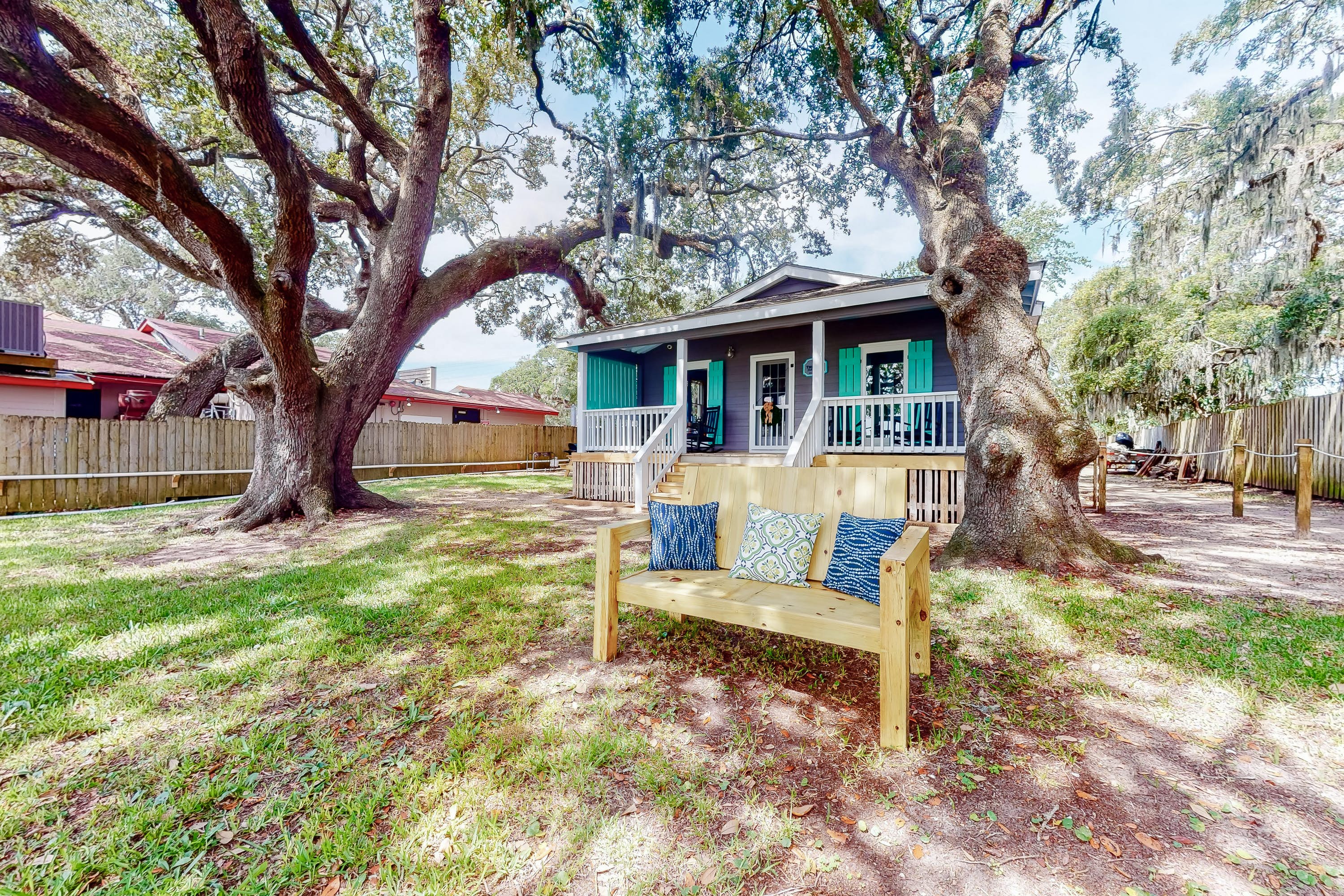 Backyard of a lodge in Litchfield, SC with two large trees and wooden bench on a sunny day.