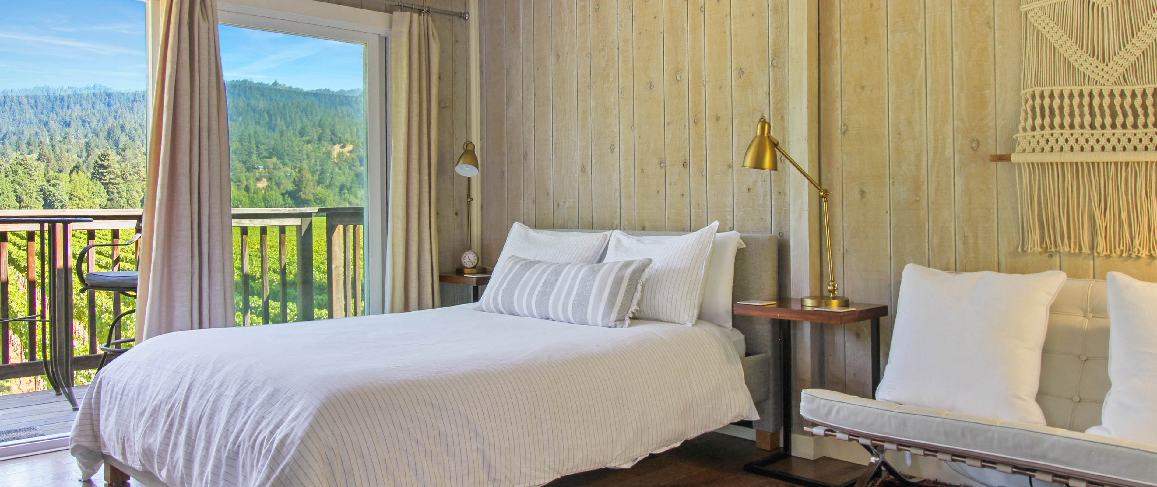 Inside a Guerneville, CA vacation rental bedroom with wooden wall panels and balcony overlooking a forest.