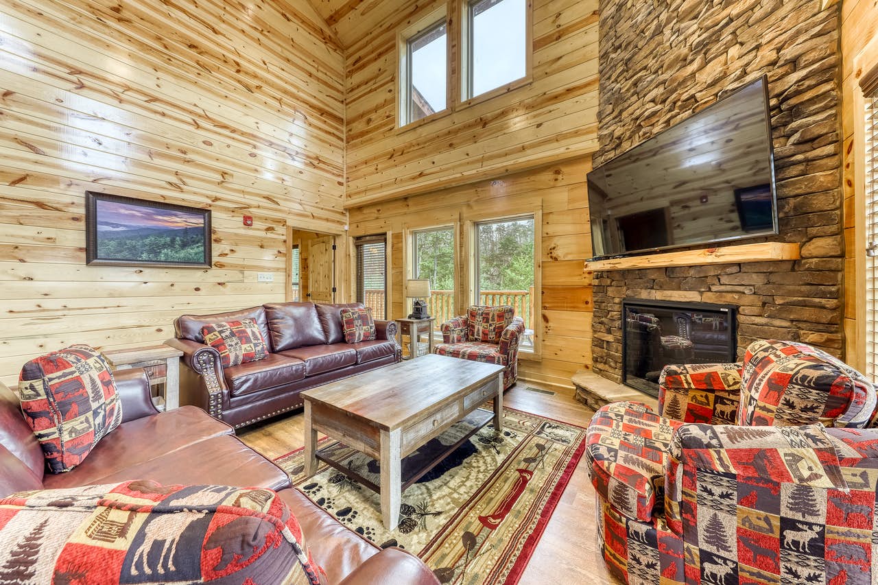 vacation cabin with stone fireplace and large flat screen tv surrounded by rustic couches
