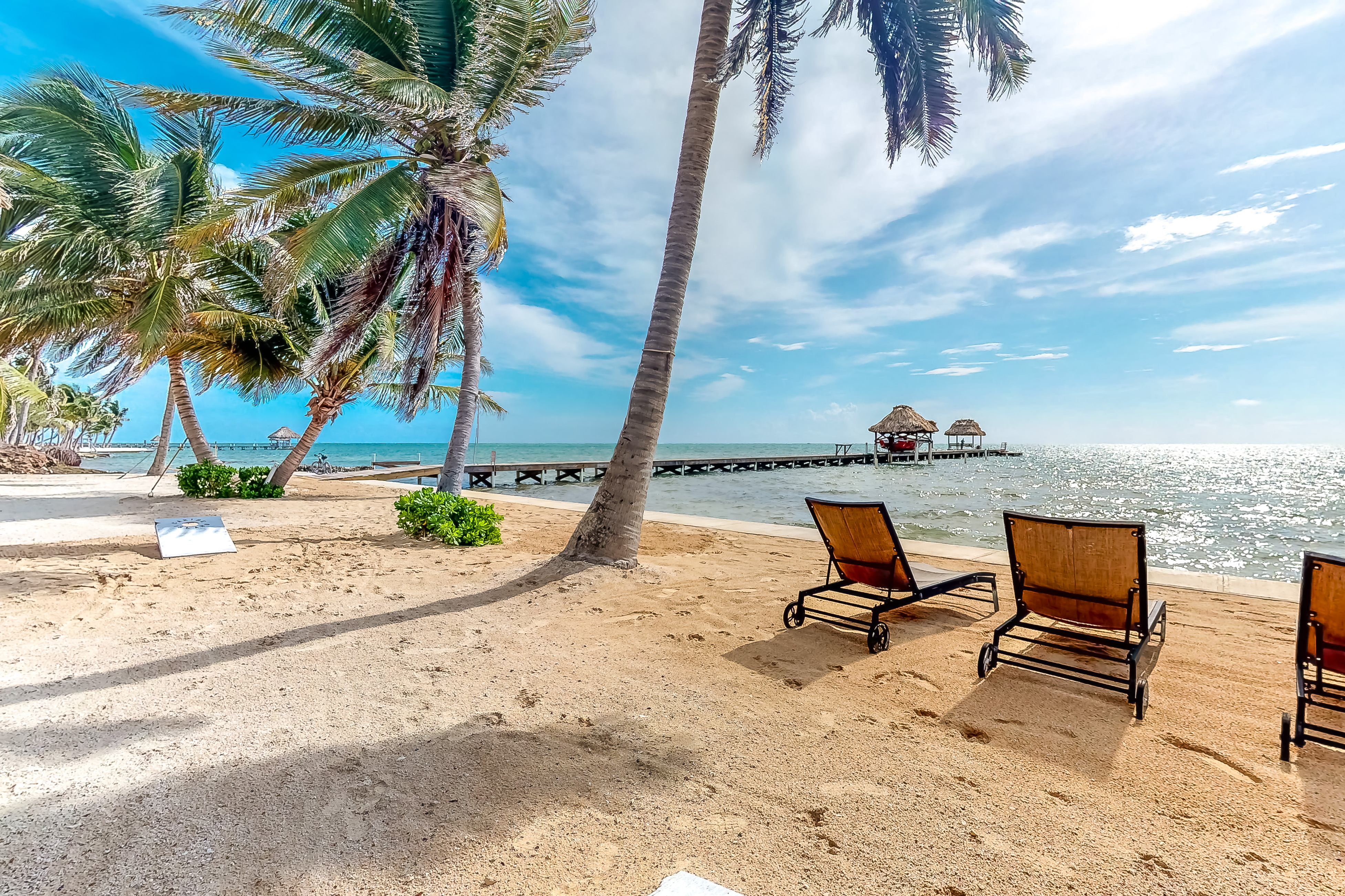 Lounge chairs on a the beach under palm trees overlooking the ocean with a dock in the foreground at a vacation rental in Belize,