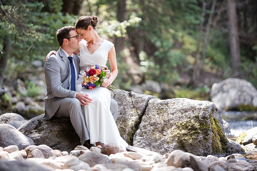 Couple sitting on a rock near a creek wearing wedding attire at Lion Square Lodge.