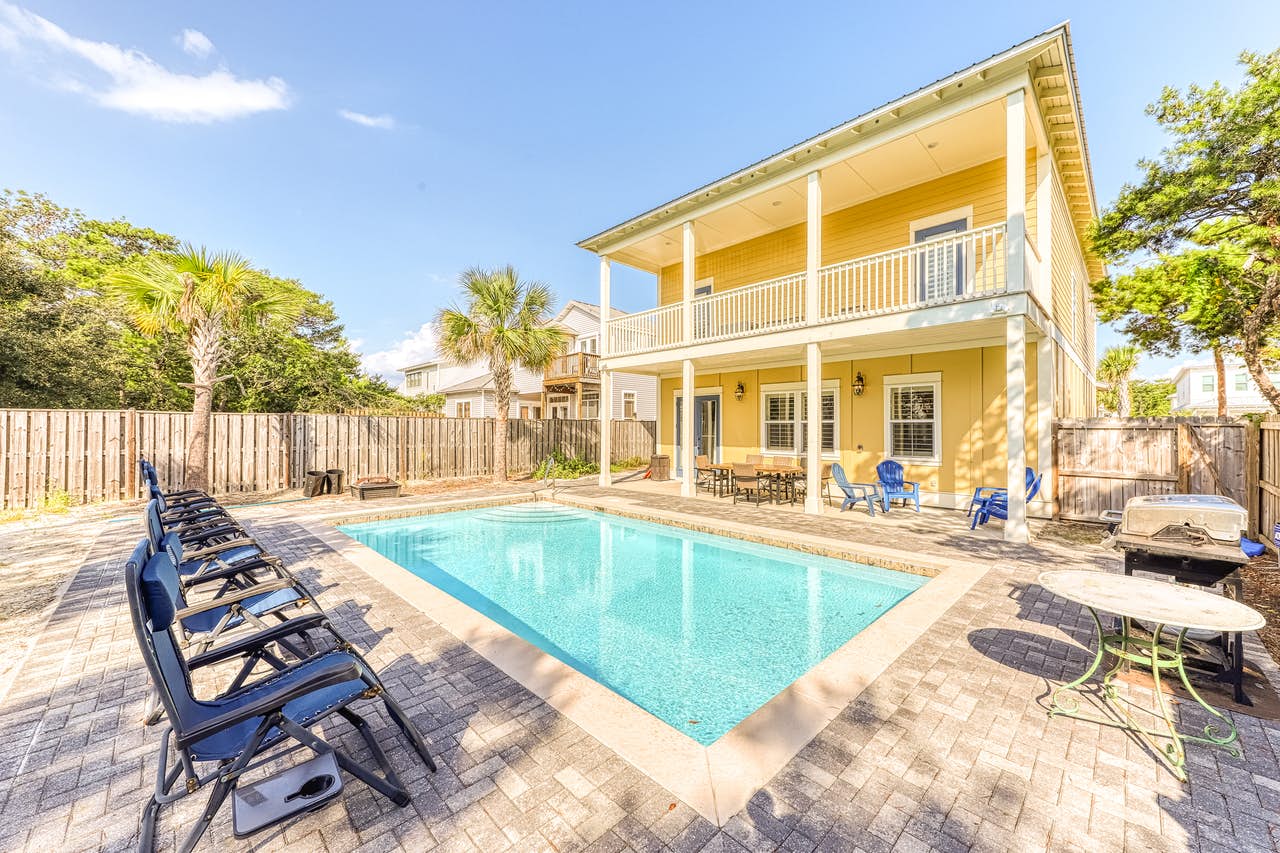 A vacation rental in Destin, FL with an outdoor pool in the backyard with barbecue setup and pool chairs.