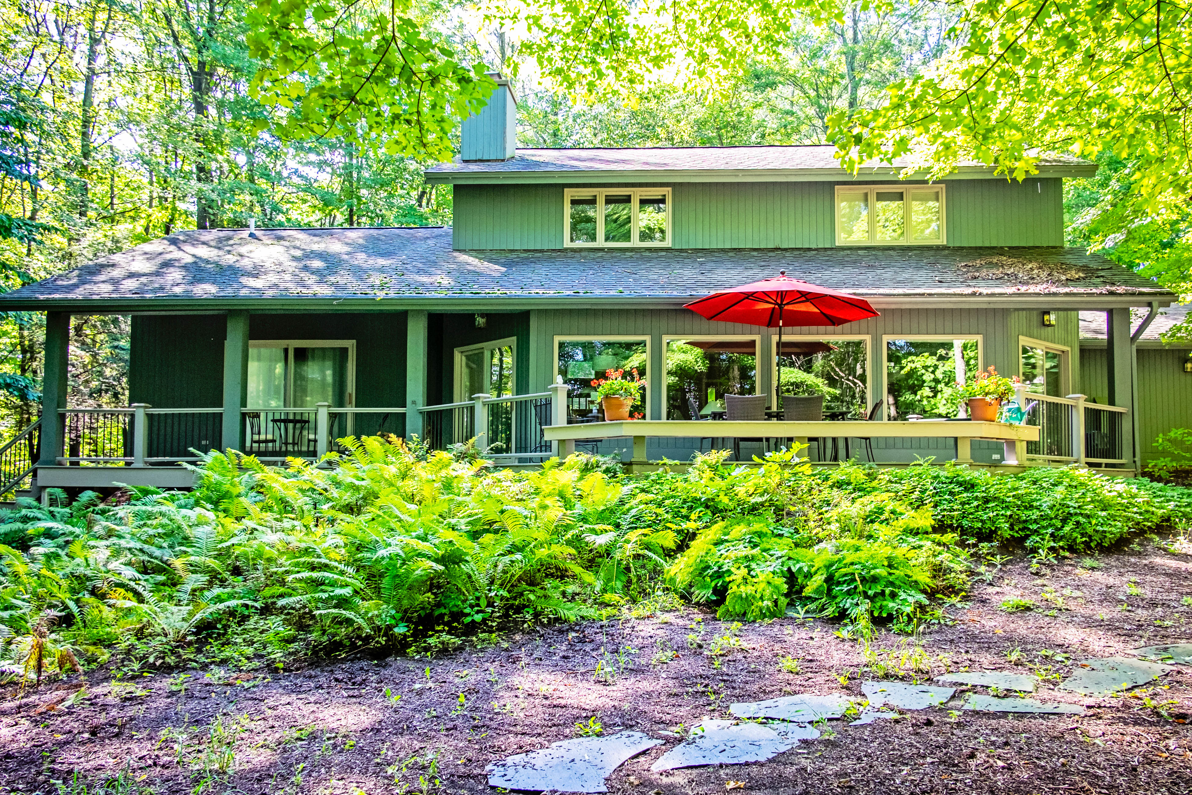 Vacation home with wraparound deck surrounded by large green trees and ferns in Harbor Springs, MI