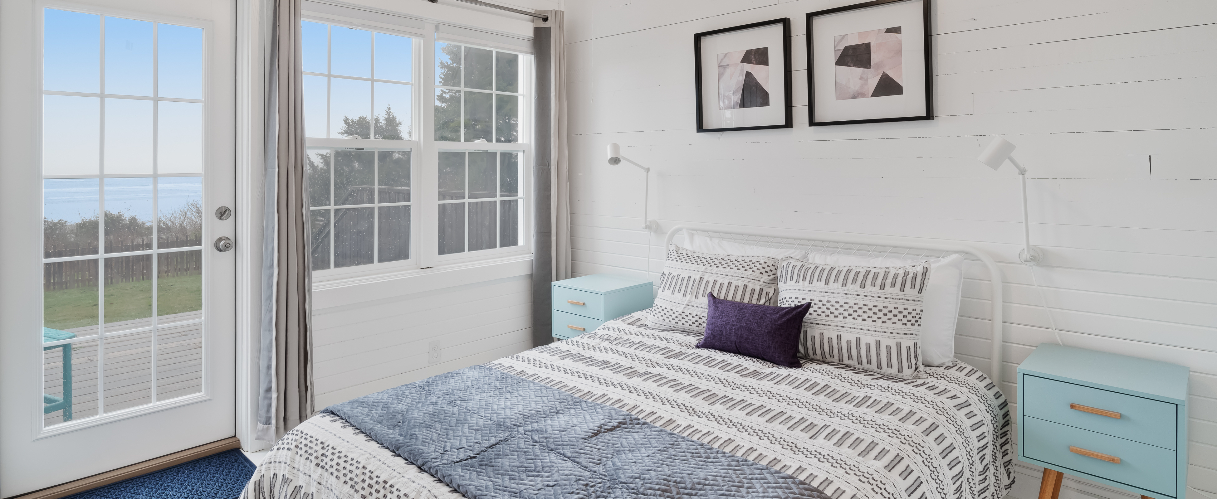 Inside a bedroom of a Moclips, WA vacation rental with white walls and queen sized bed and a view of the ocean.
