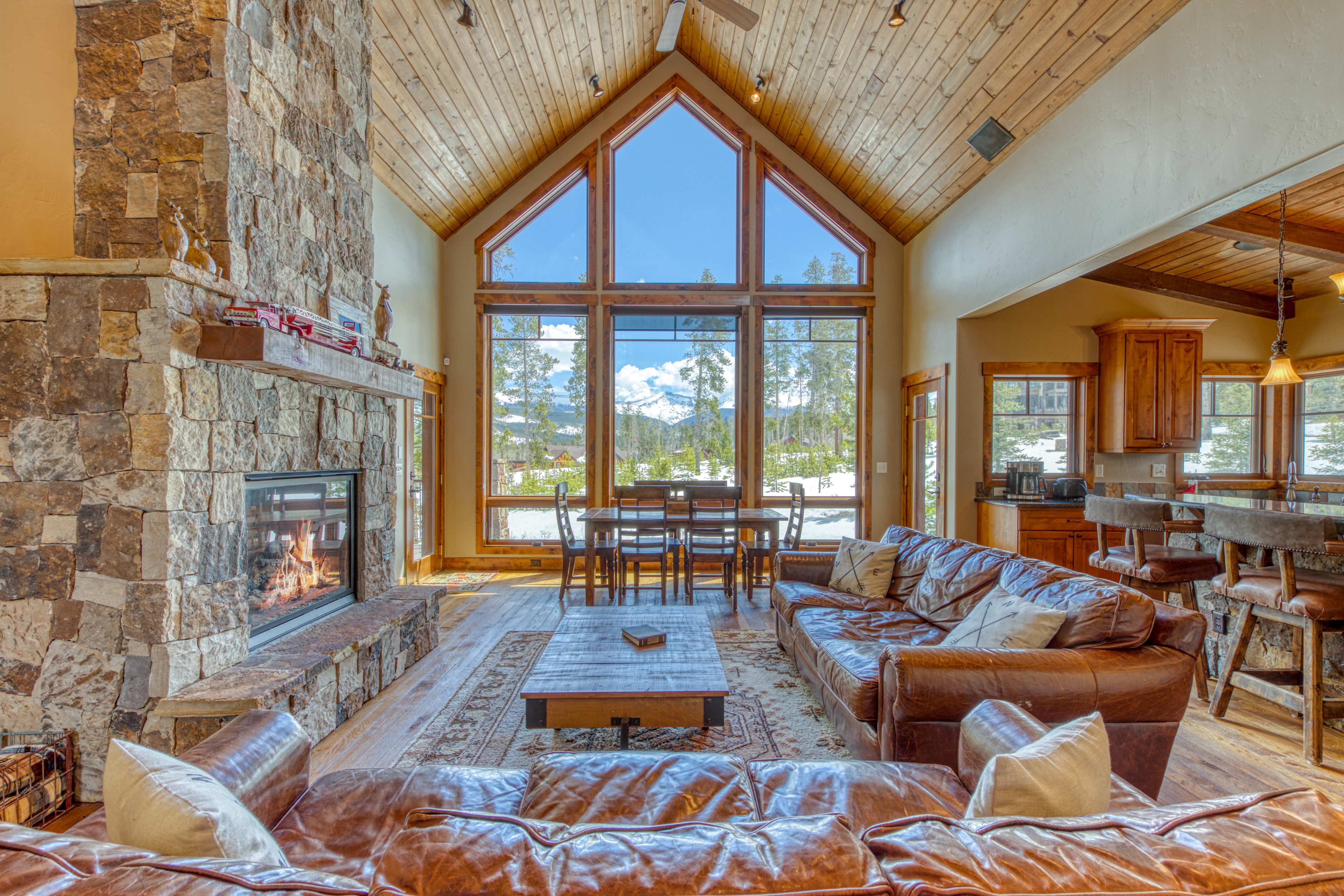 living room with leather couches large mountain-view windows and a stone fireplace