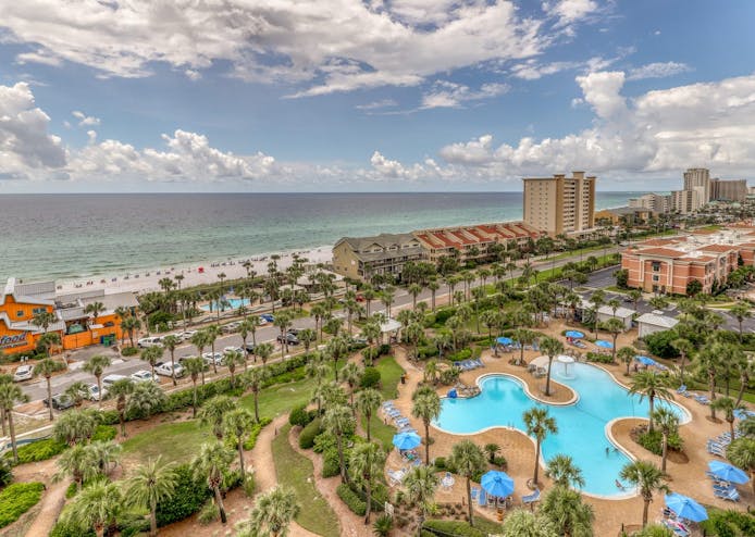 A view of Destin, FL overlooking the shore, city, main road and large outdoor pool.