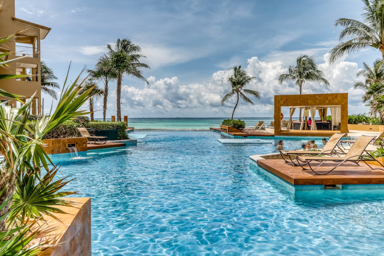 A pool overlooking the ocean with chairs and cabanas at a resort in Mexico.