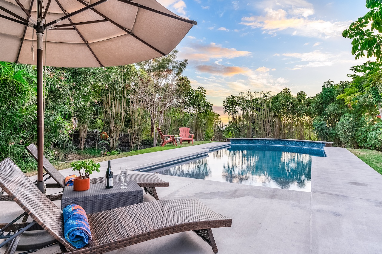Two chairs with a wine bottle and glasses near a pool at a vacation rental in Kailua-Kona, HI.