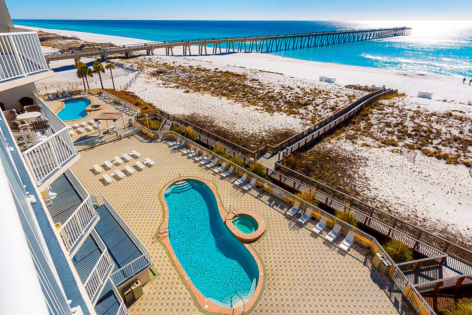 View of the ocean overlooking the ocean, a pool, and the pier of Navarre Beach from the patio of a resort.