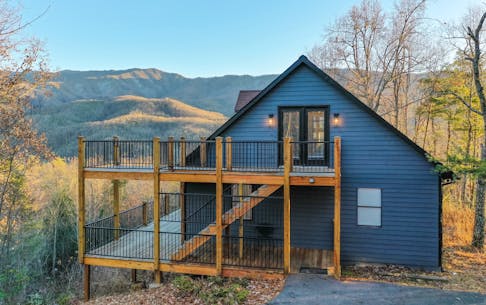 Blue vacation home rental in Gatlinburg, TN with wooden balconies on two stories alongside the house in the woods.