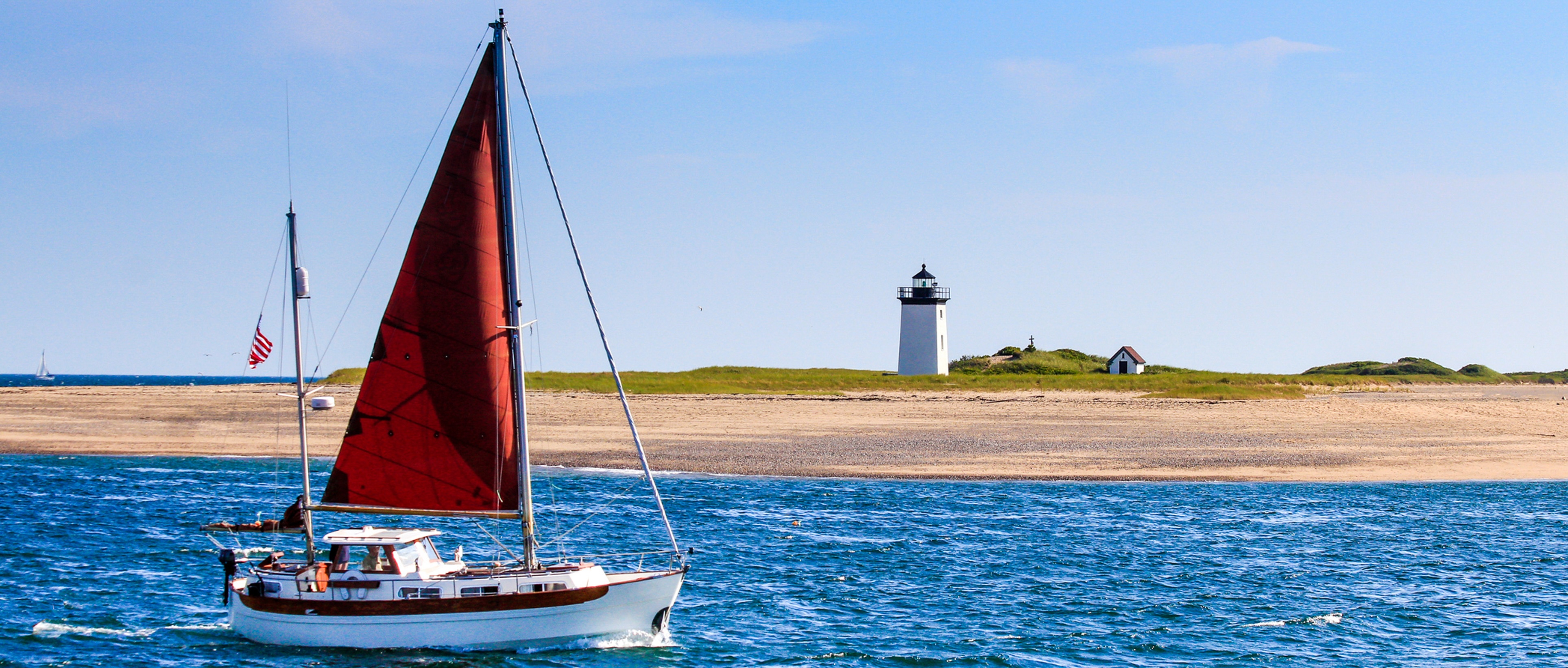 Boat on the waters of Cape Cod with a lighthouse in the background.
