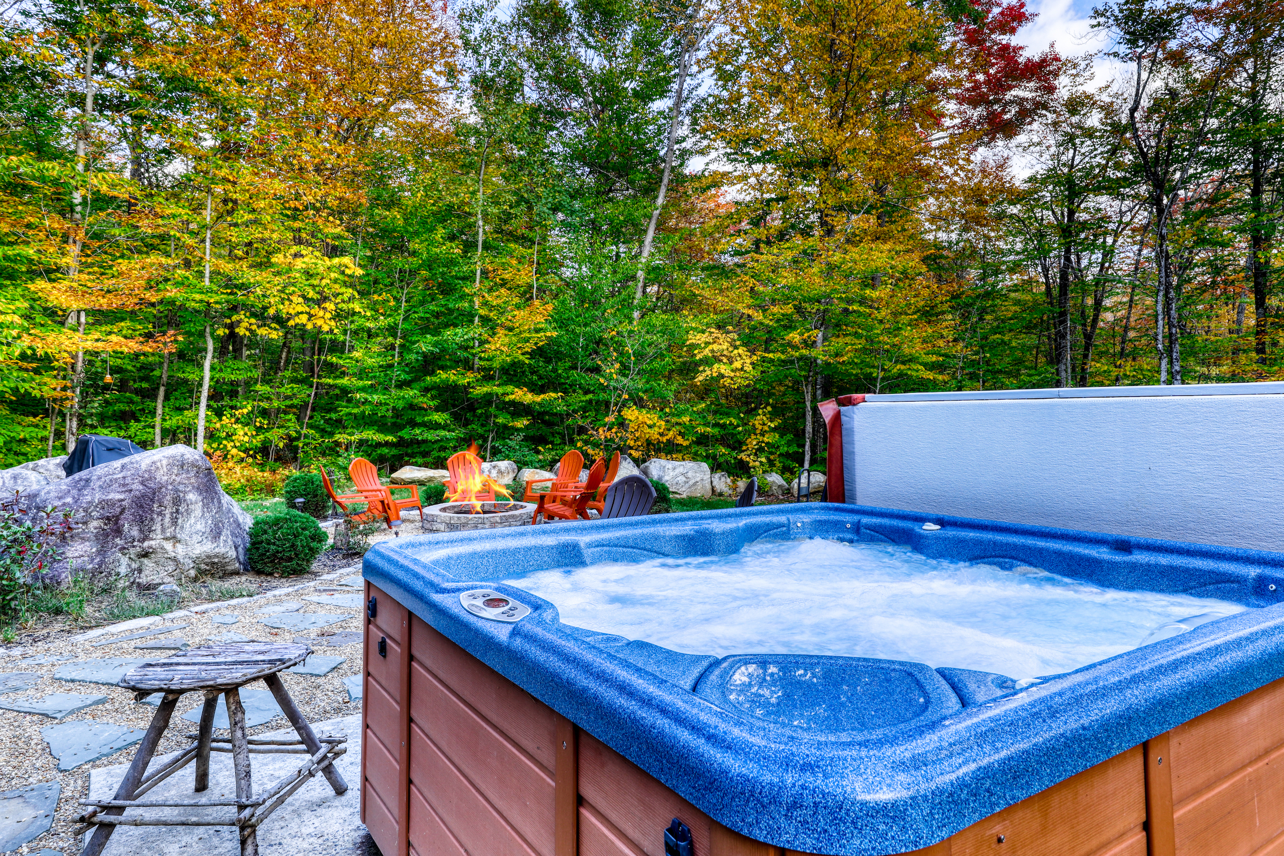 private outdoor hot tub sits near a firepit in backyard of Greenwood, ME vacation home