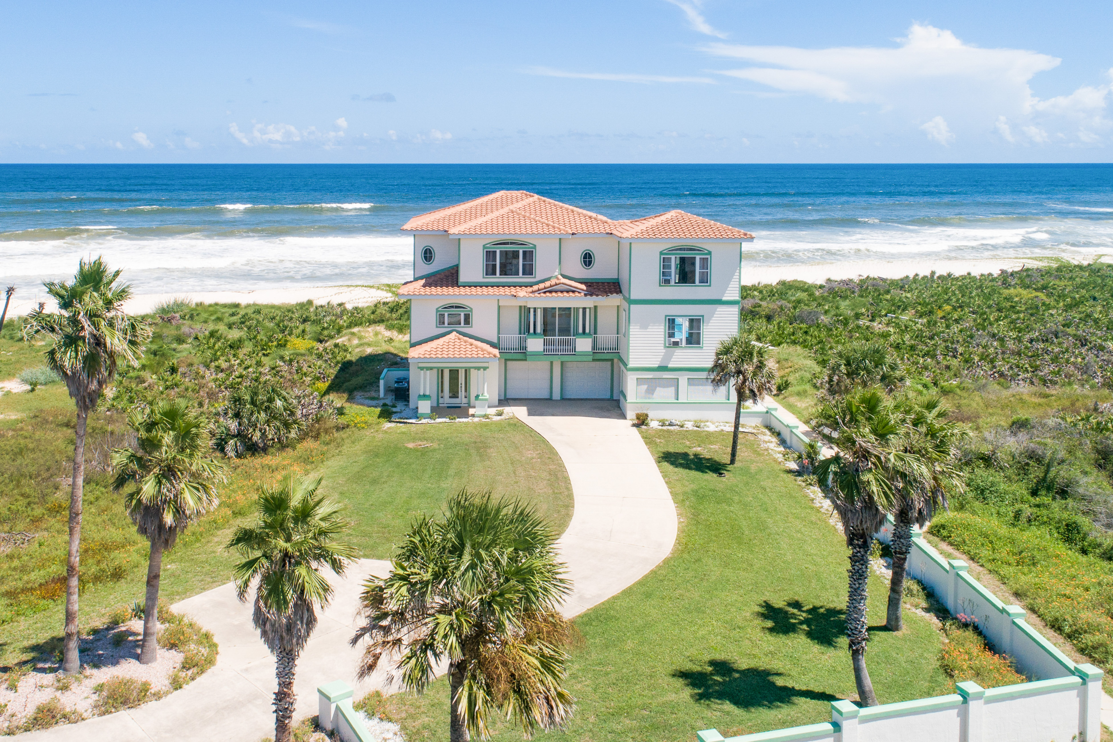 large white, oceanfront vacation home surrounded by palm trees