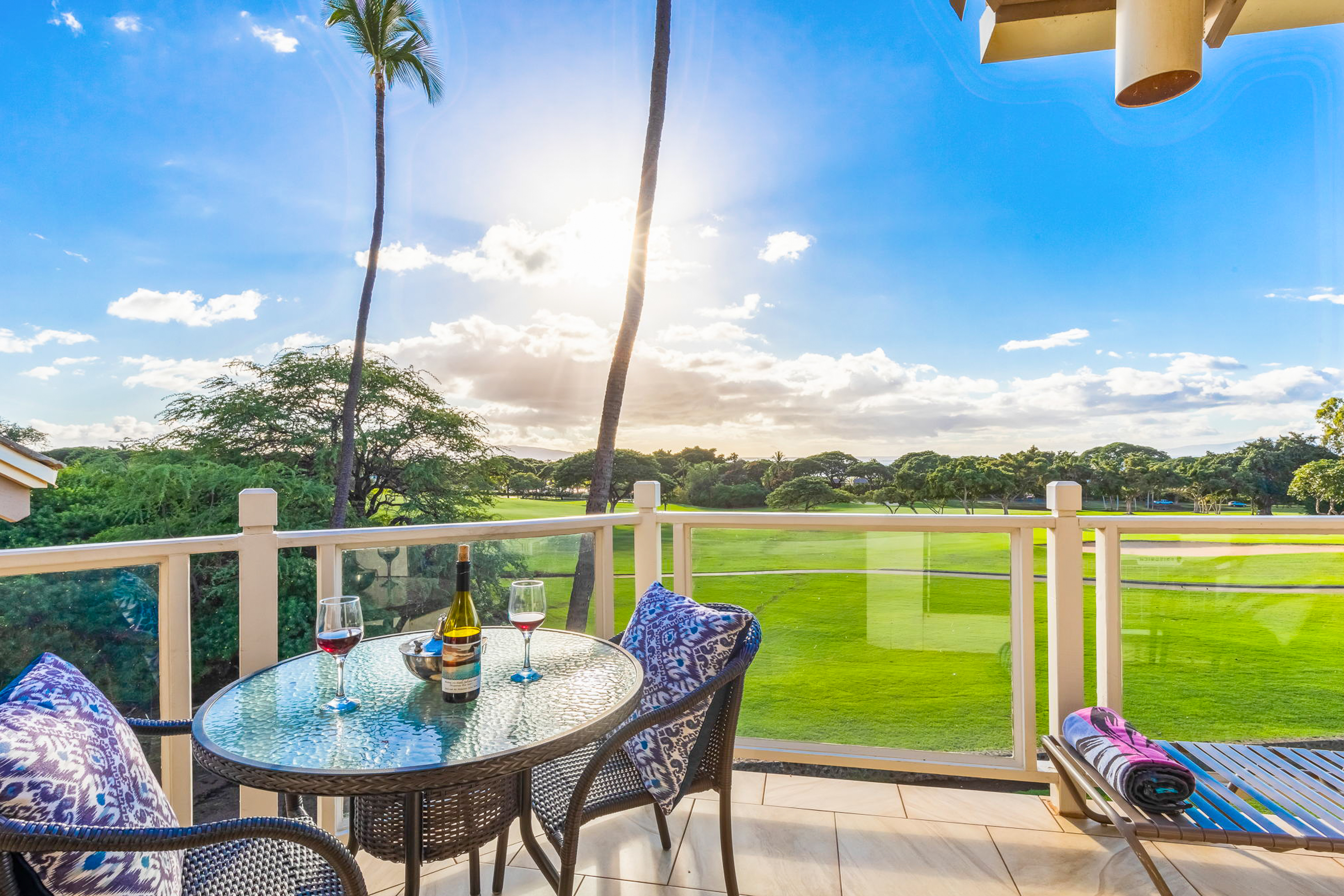 a table set with two glasses of wine on balcony overlooking golf course in maui