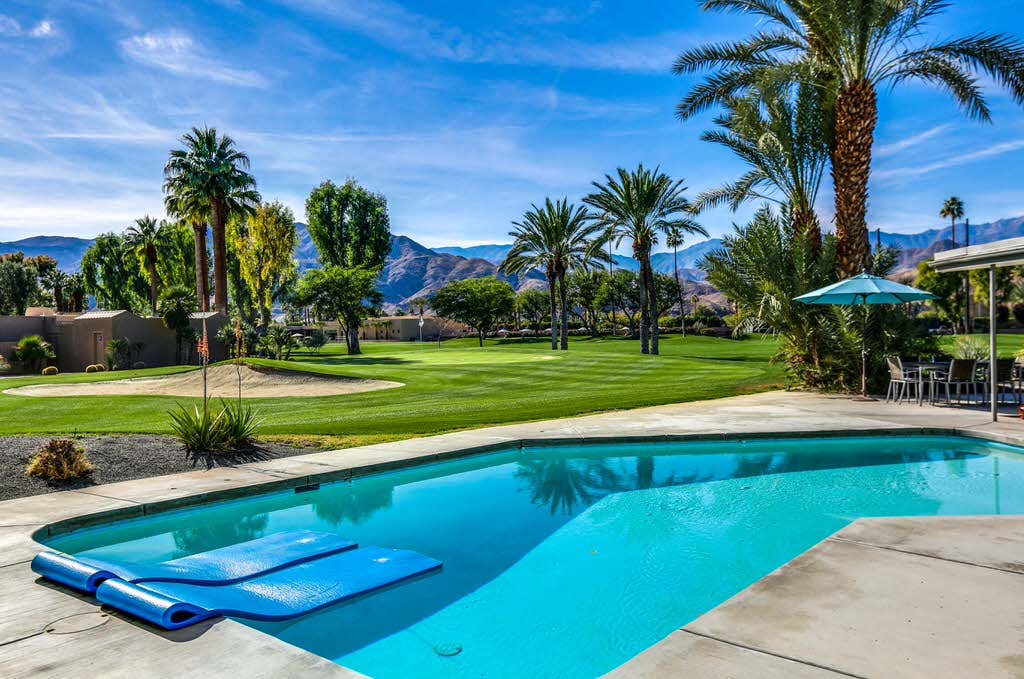 An outdoor pool near a golf course with palm trees in Coachella Valley, CA.