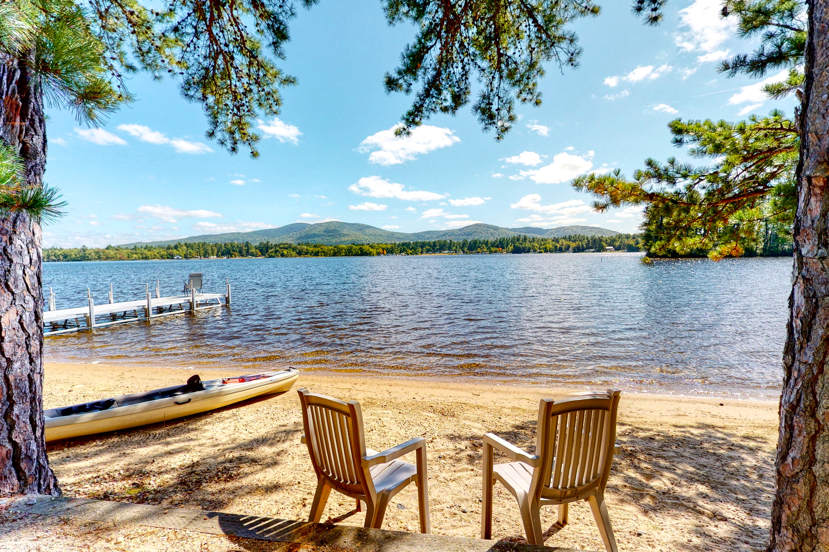 Chairs and kayak sit on the sand in Ossipee, NH facing water and dock