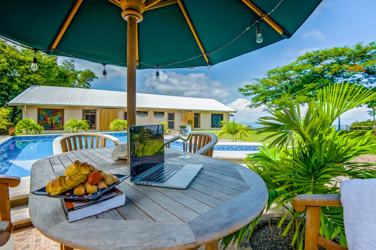 a laptop and wine glass sit on a patio table overlooking the private outdoor pool in Costa Rica vacation home
