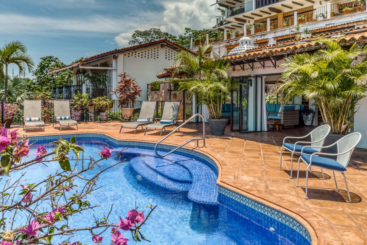 Blue outdoor pool at a vacation rental with lounger chairs and palm trees.