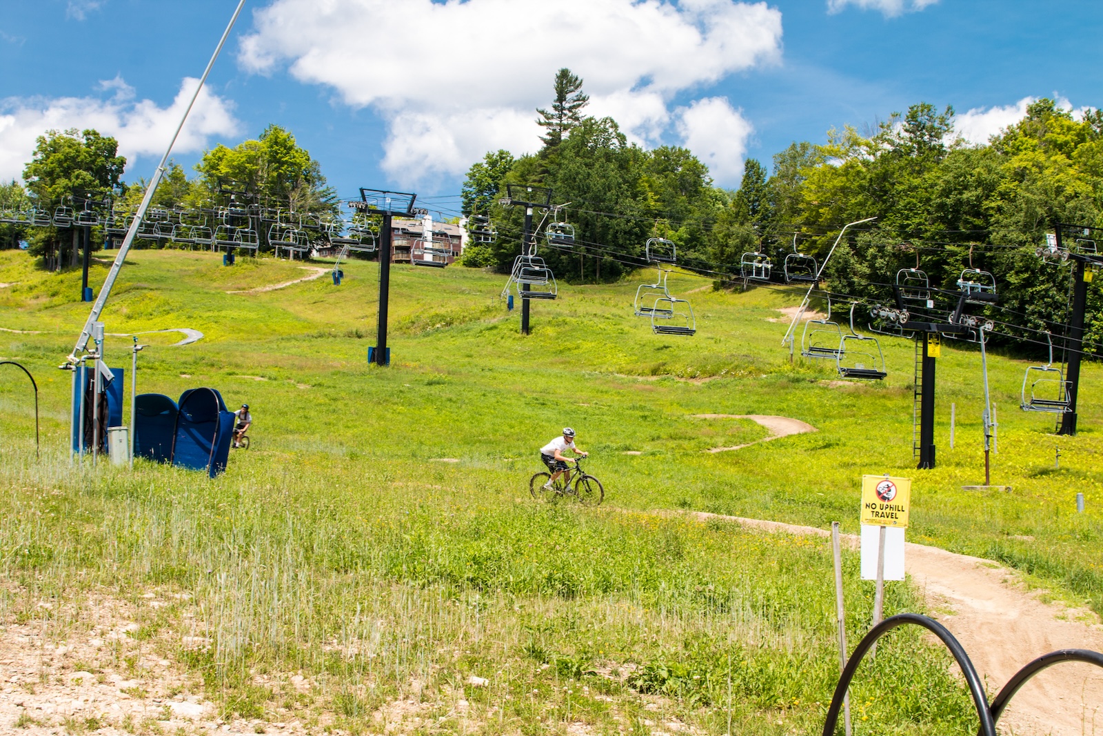 Bikers bombing down a route near a ski lift.