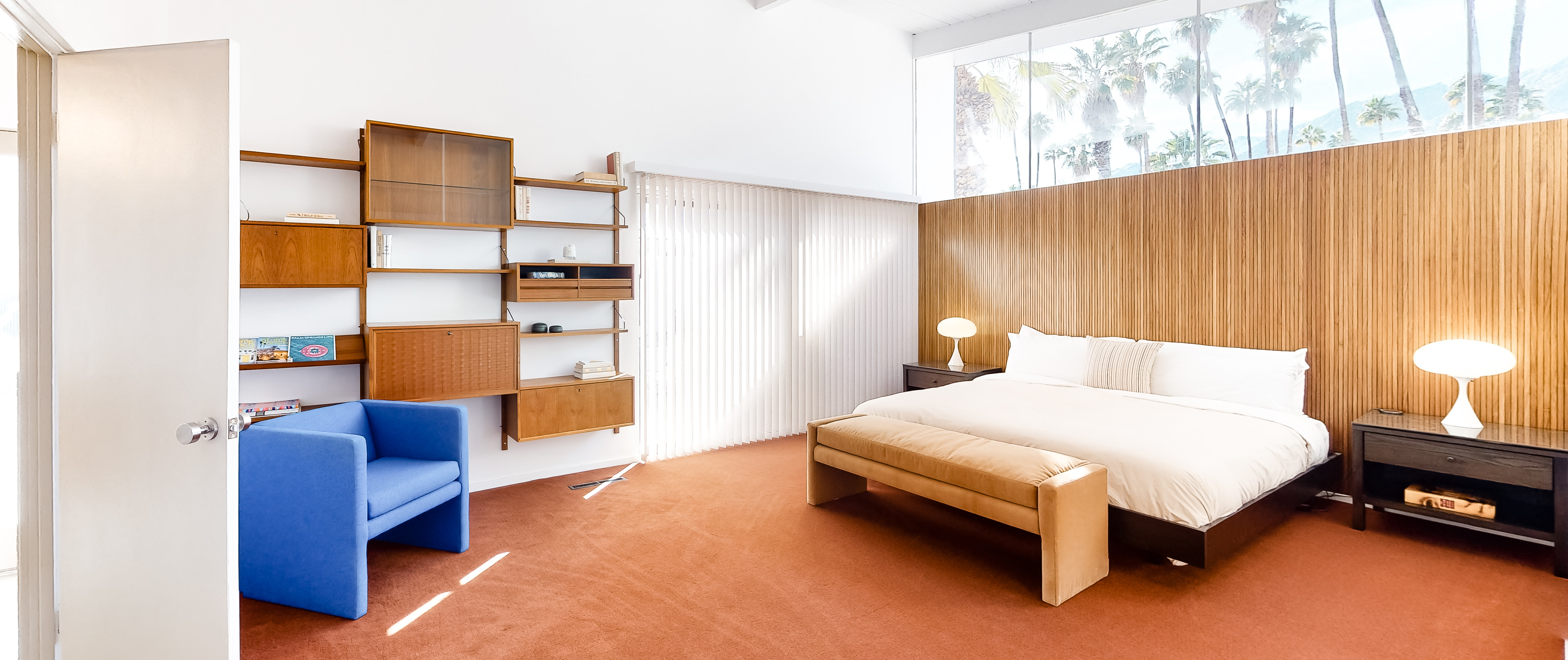 Inside a Palm Springs, CA vacation rental bedroom with large open space, white bed and hanging shelves.