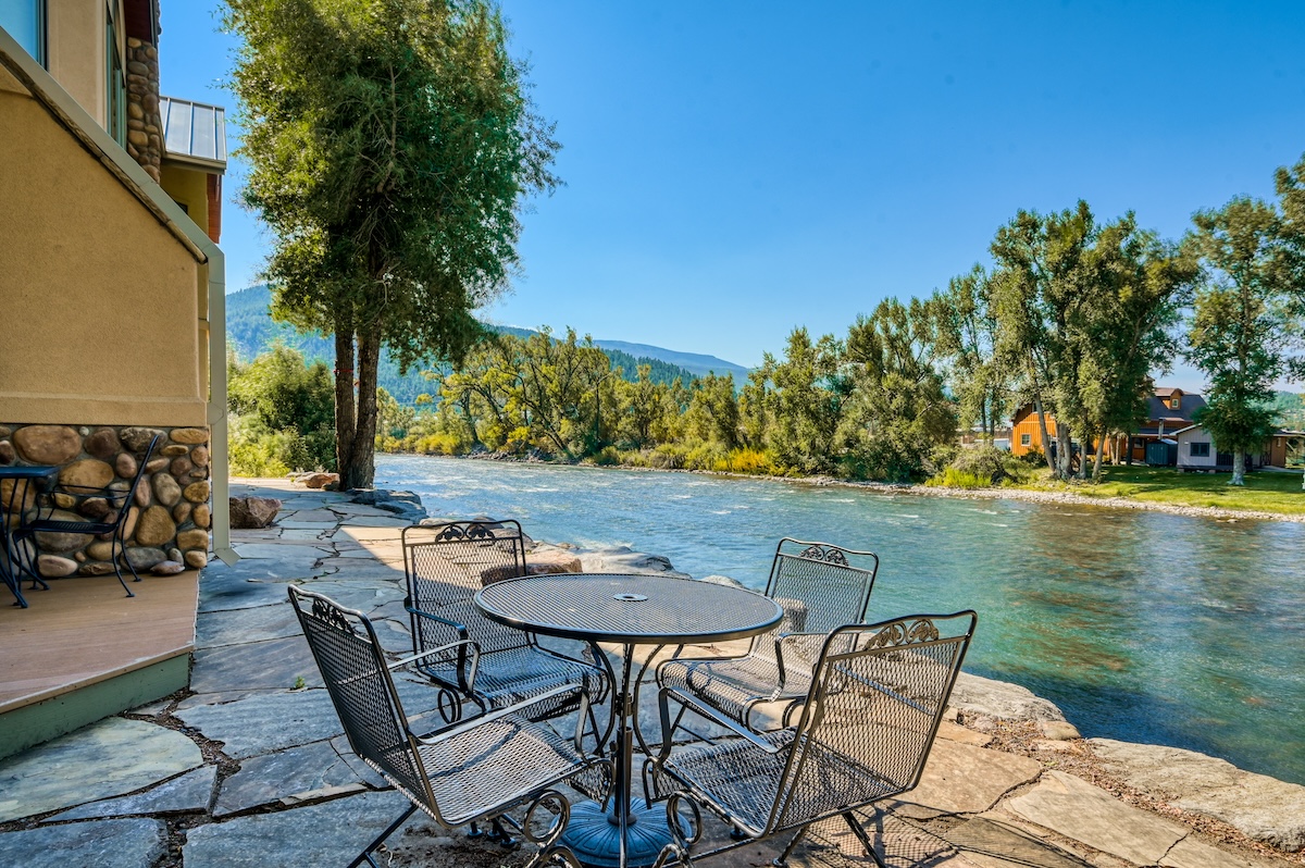 View of the river on a patio with chairs and a table.