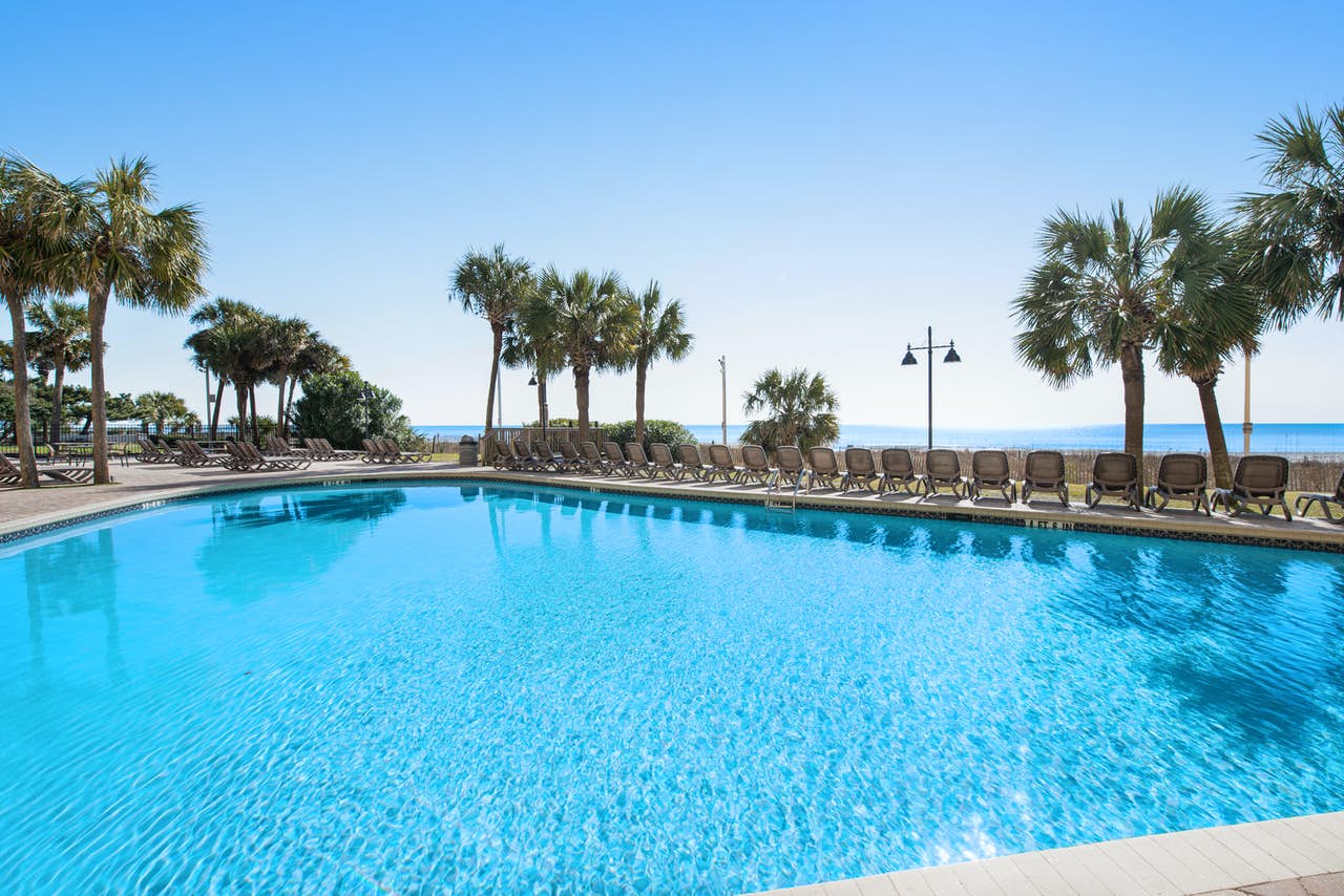 Large pool with clear blue water and a long row of outdoor pool chairs facing the beach in Myrtle Beach, SC.