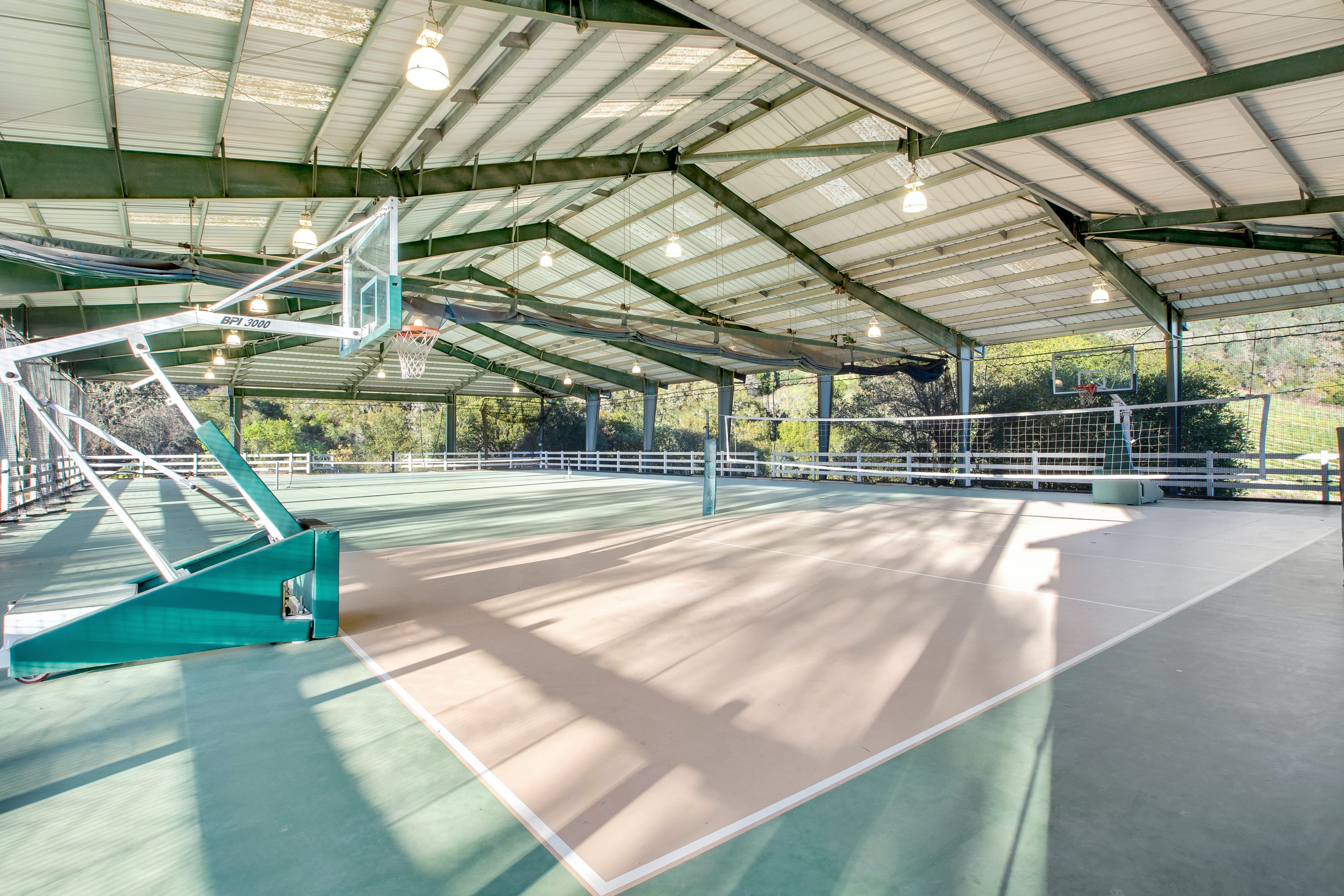 covered sports court with a tennis net and basketball hoop