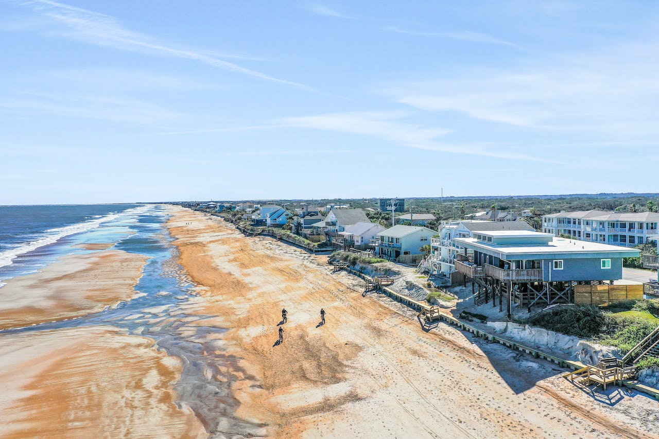 Drone shot of a people walking on the beach with the ocean to the left and houses to the right.