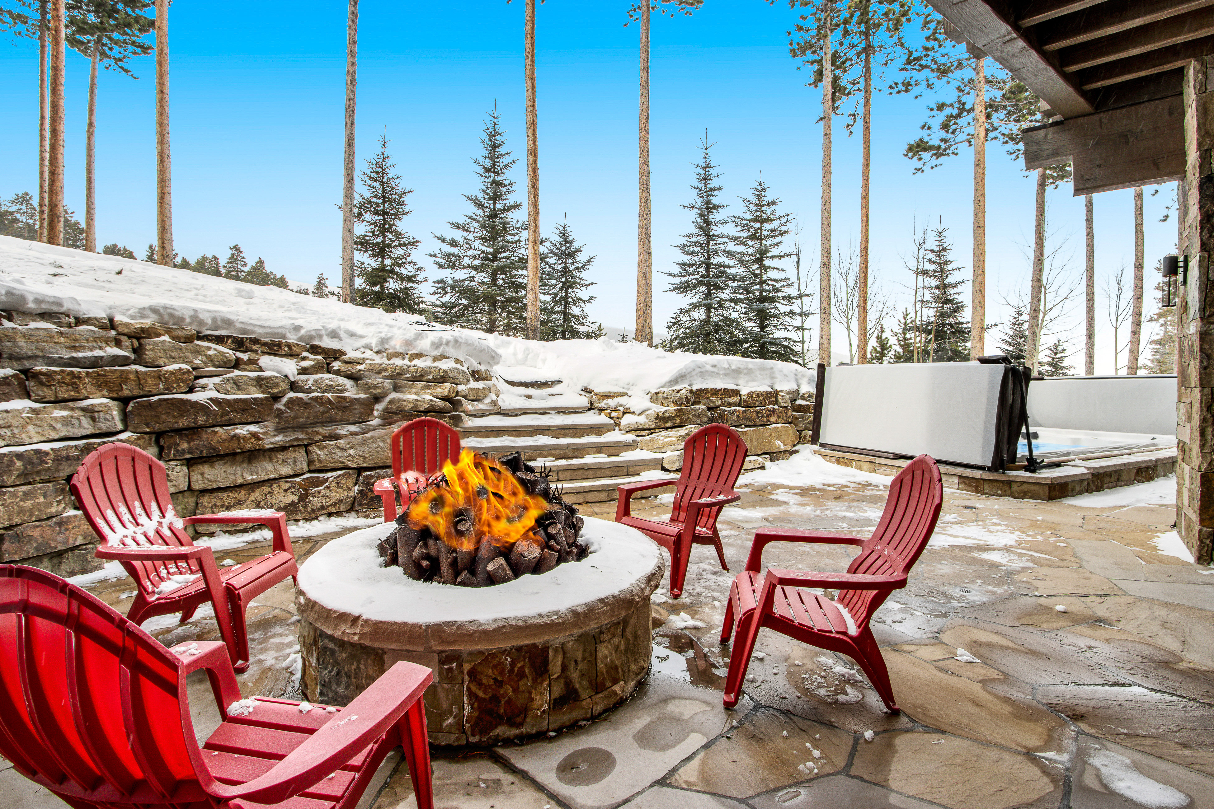 outdoor fire pit with fire and chairs with snow in the background