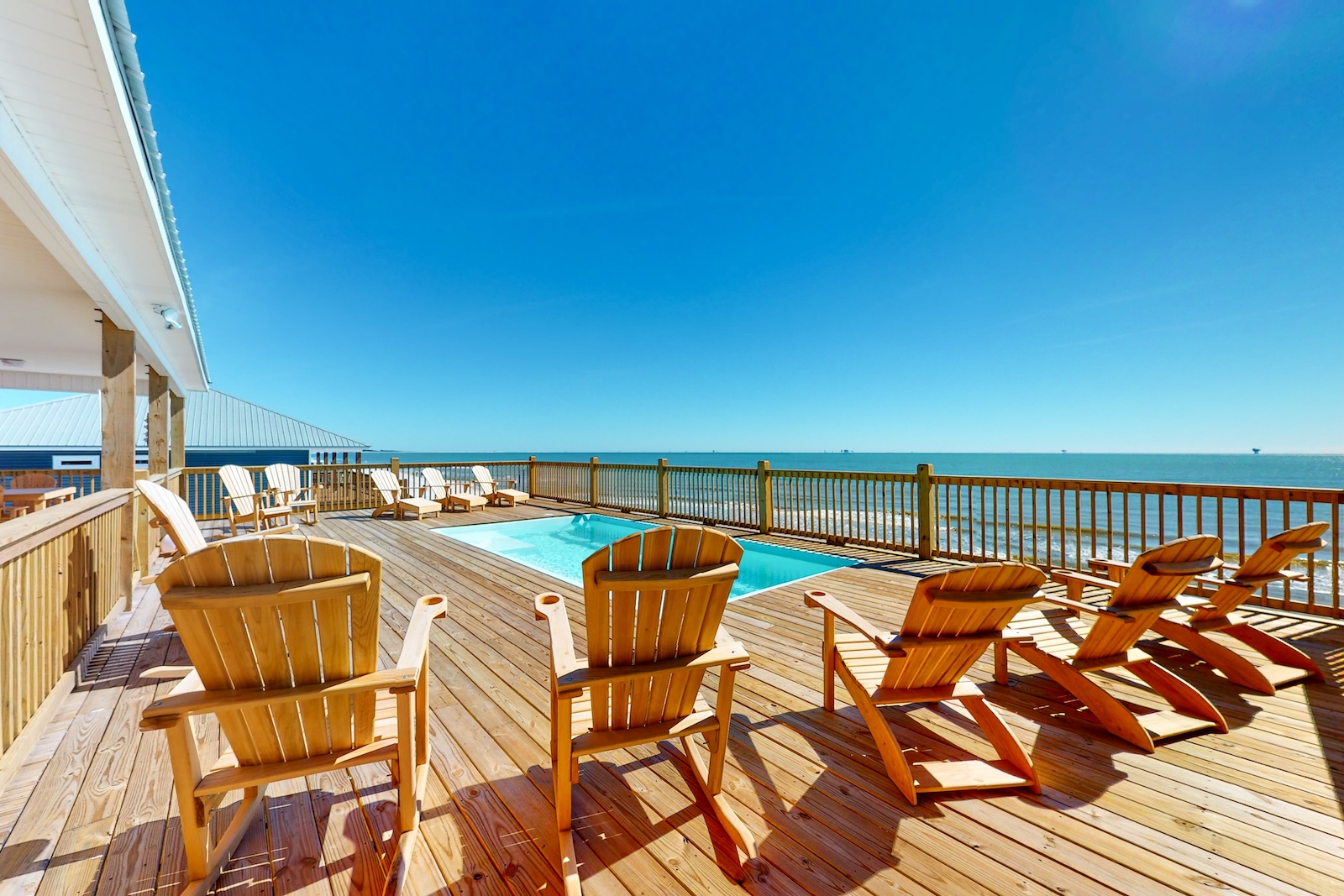 A back deck area with a pool, chairs, and a view of the ocean at a rental in Dauphin Island, AL.