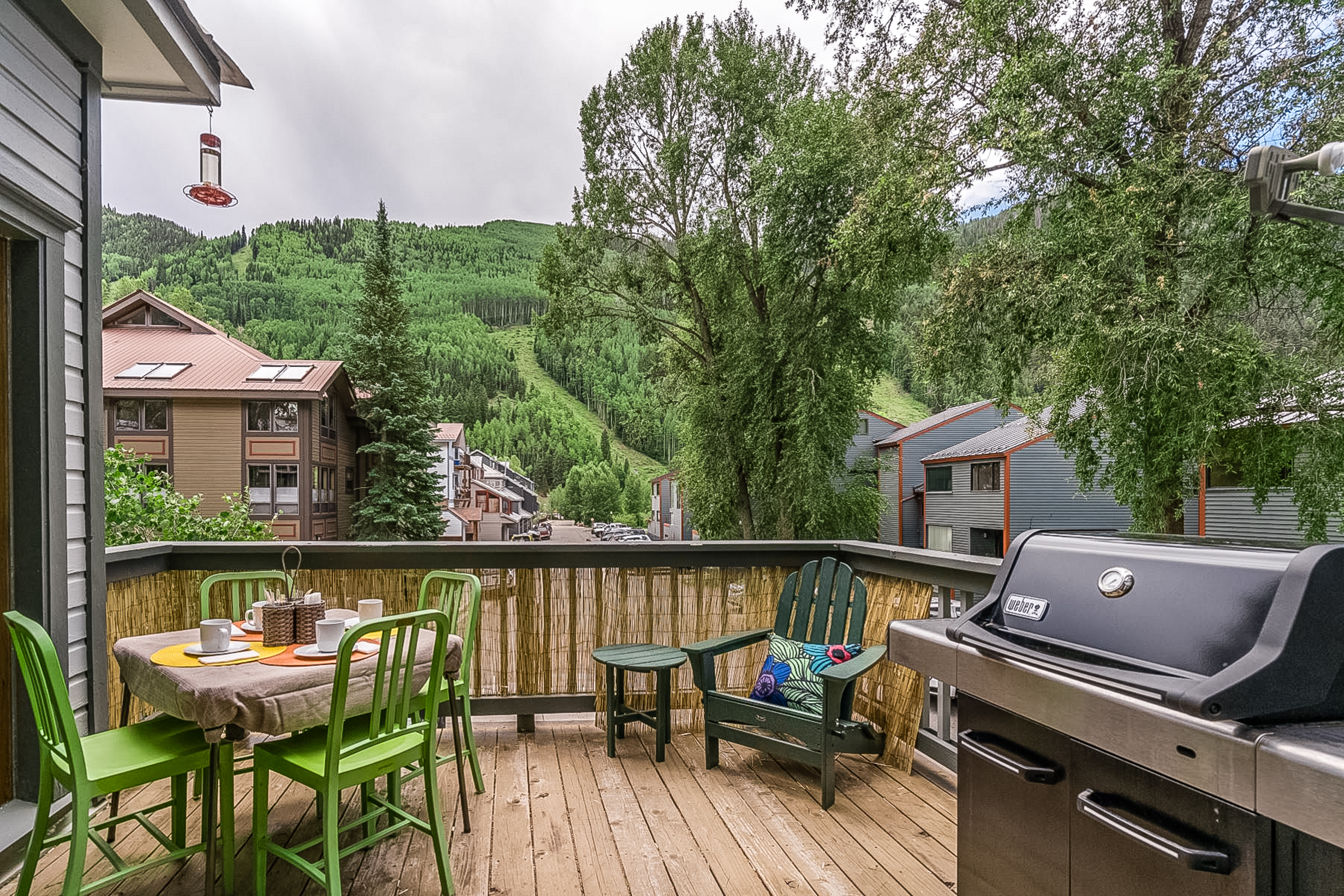 Back wooden porch of a vacation rental in Telluride, CO with tables, green chairs, and grill on a cloudy day.