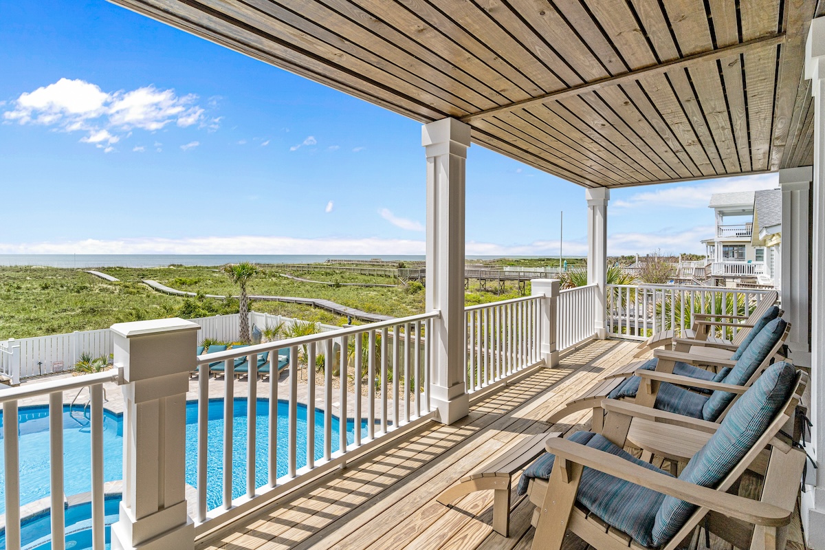 The view from a deck overlooking a pool and the coastline.