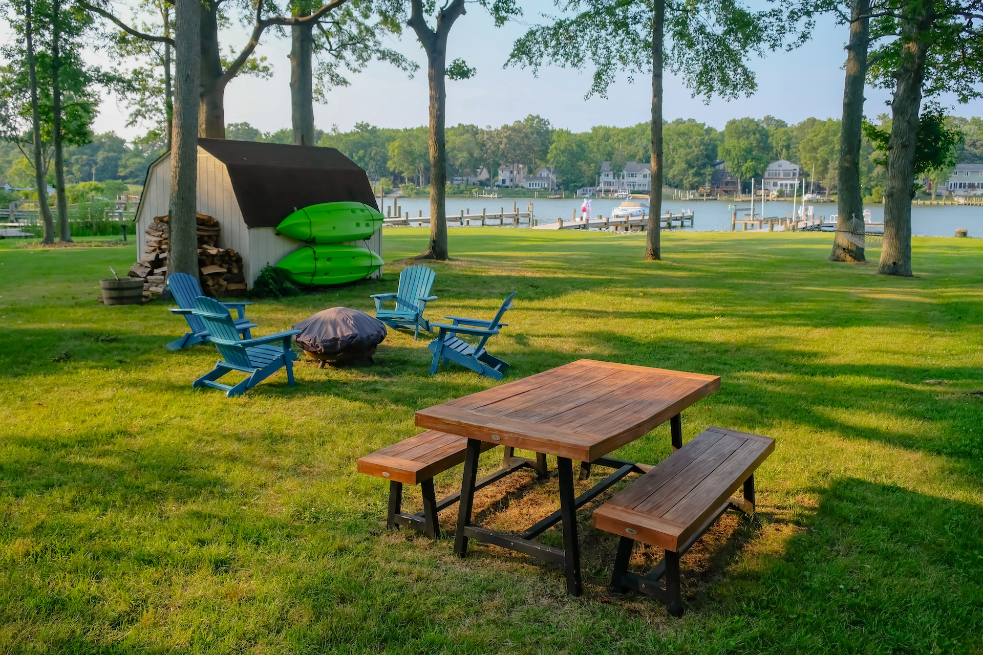 Picnic bench, a fire pit with chairs, and a shed overlooking a lake.
