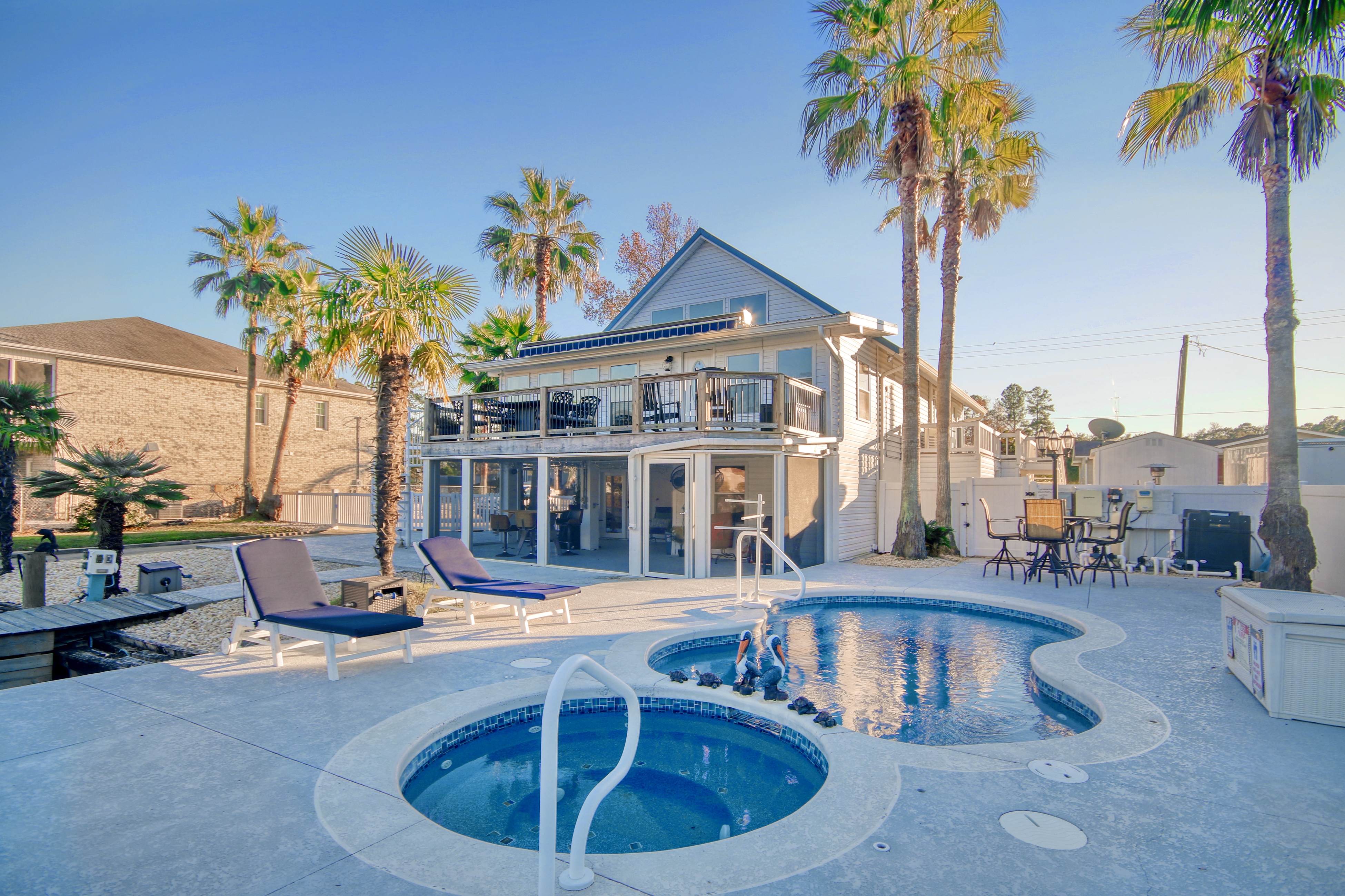 palm trees surround a vacation home with a balcony overlooking a pool and hot tub