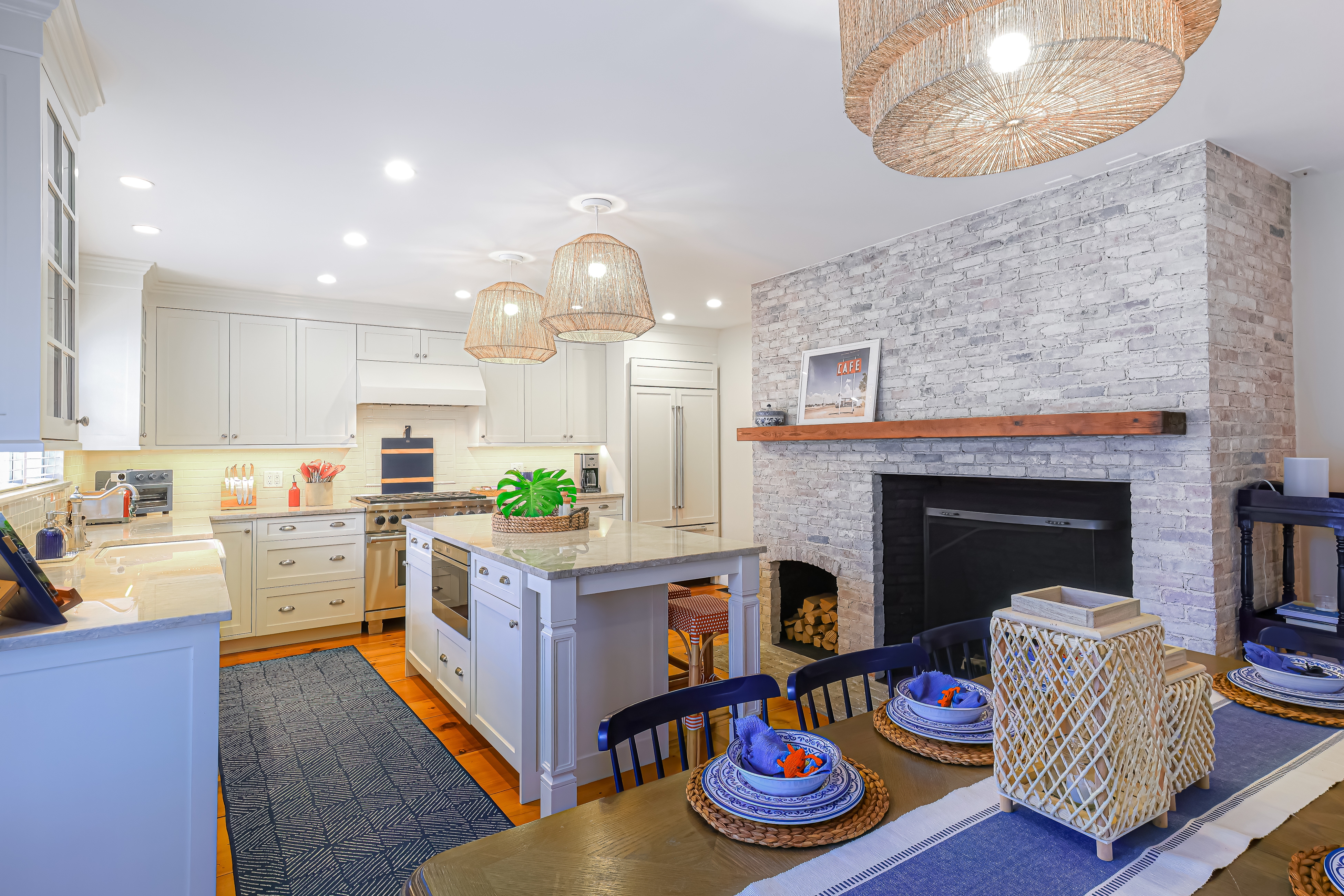 cozy living space of nantucket home with light brick fireplace, a dining table set for dinner, and clean kitchen