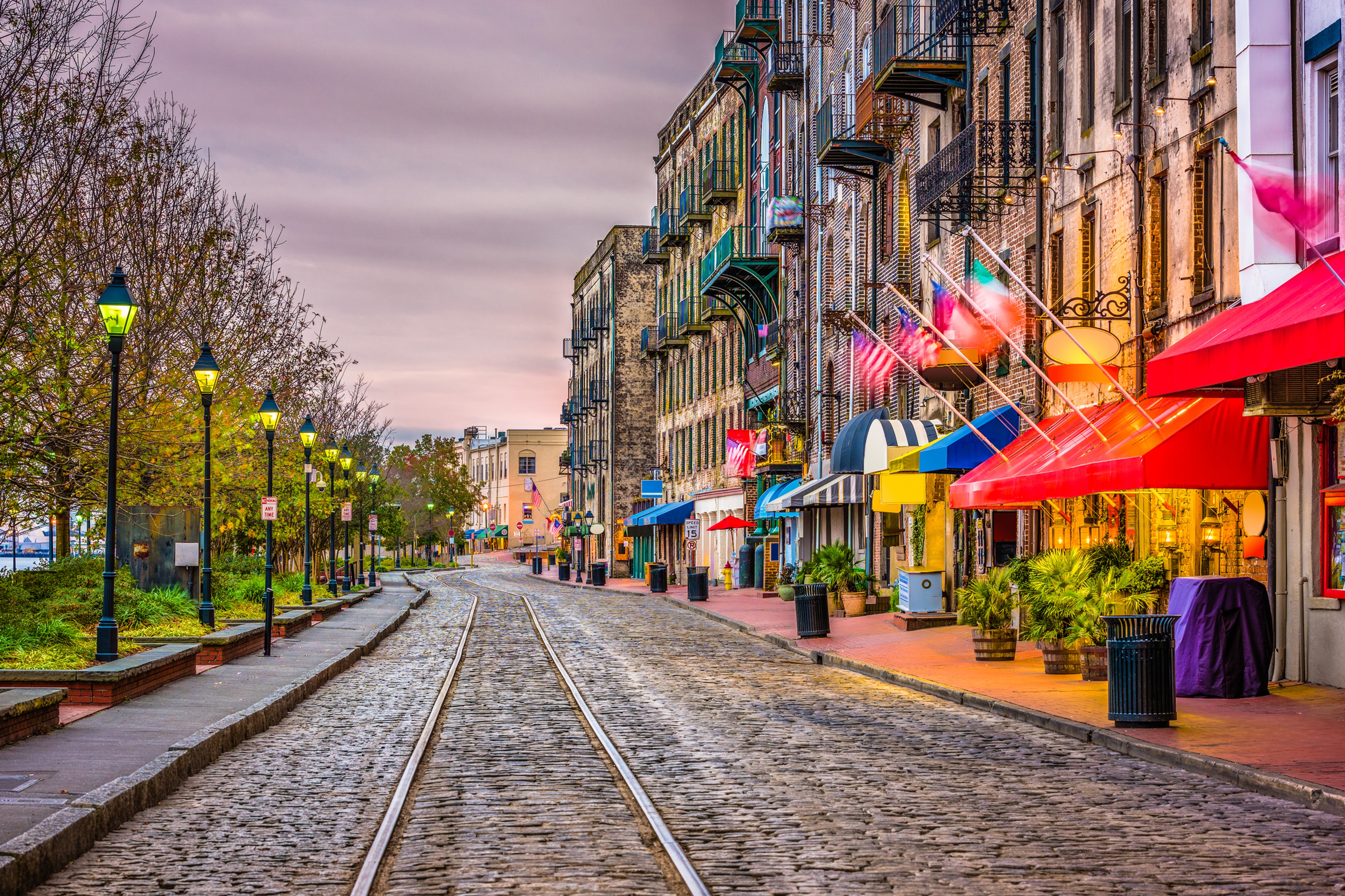 cobblestone street in savannah lined with shops beginning to light up a sunset