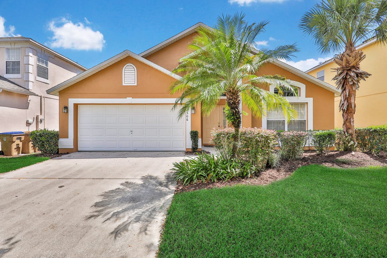 An orange single family vacation rental in Orlando, FL with a front yard with palm trees.