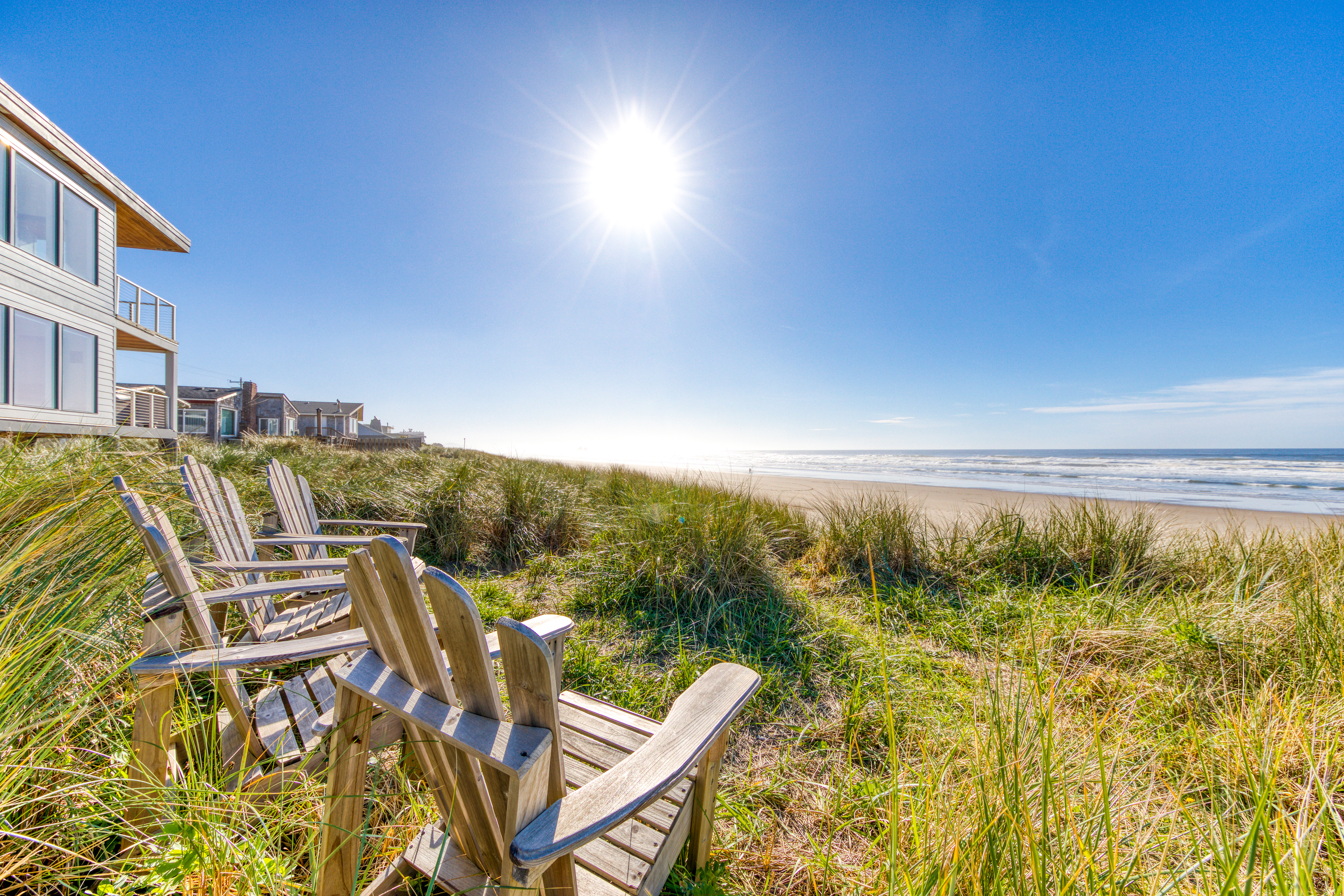 four adirondack chairs surrounded by beach grass face the ocean in Rockaway Beach, OR