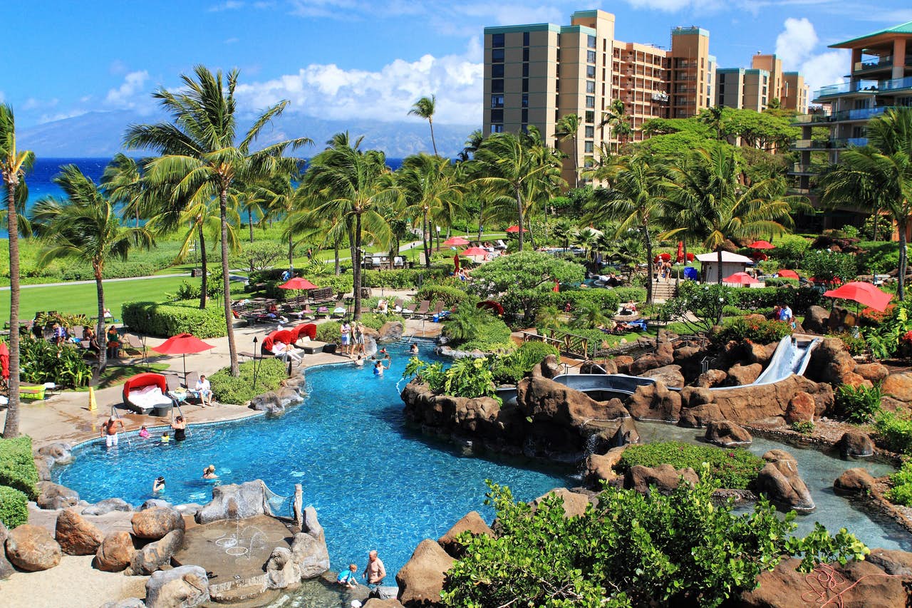 Island style outdoor pool with water slides and palm trees at a resort in Hawaii.