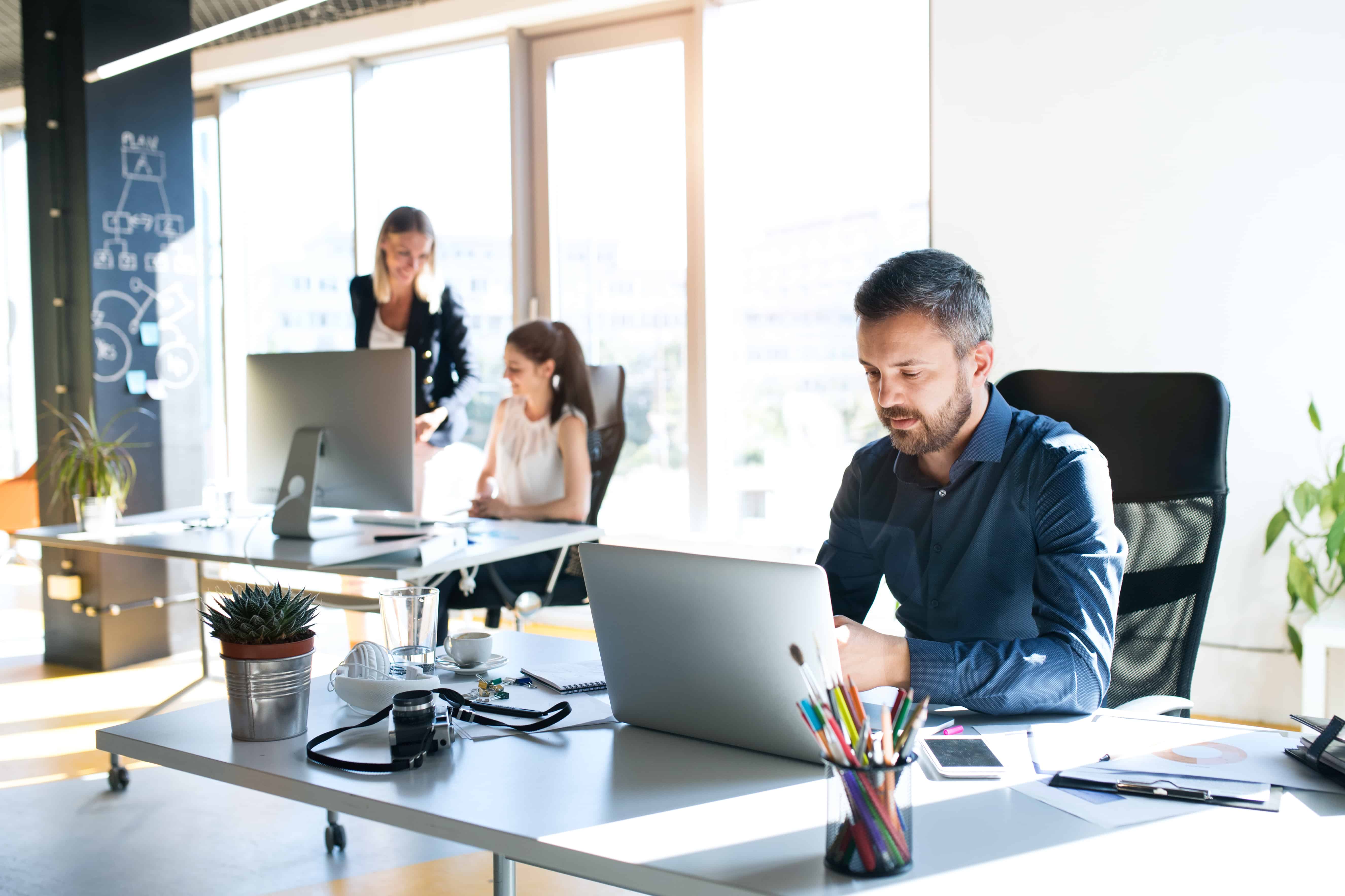 3 people sitting at their desks in a modern office space