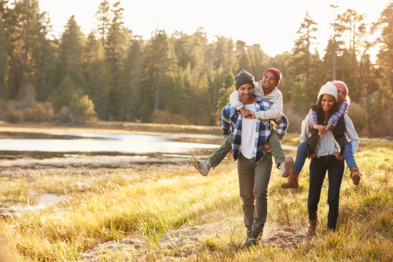 parents carrying kids on their back walking on a trail alongside a river
