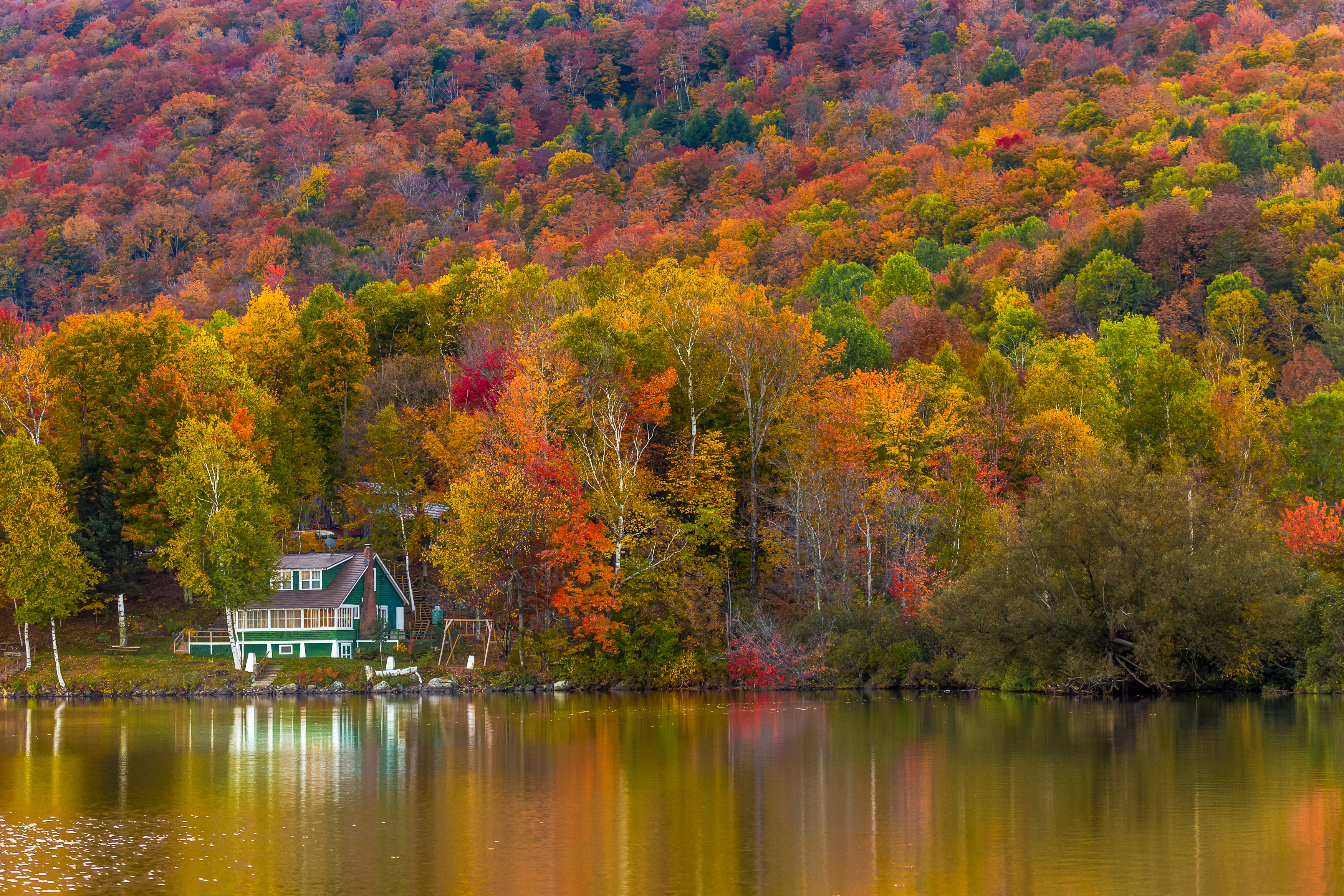green lake house by the shore surrounded by fall colored trees