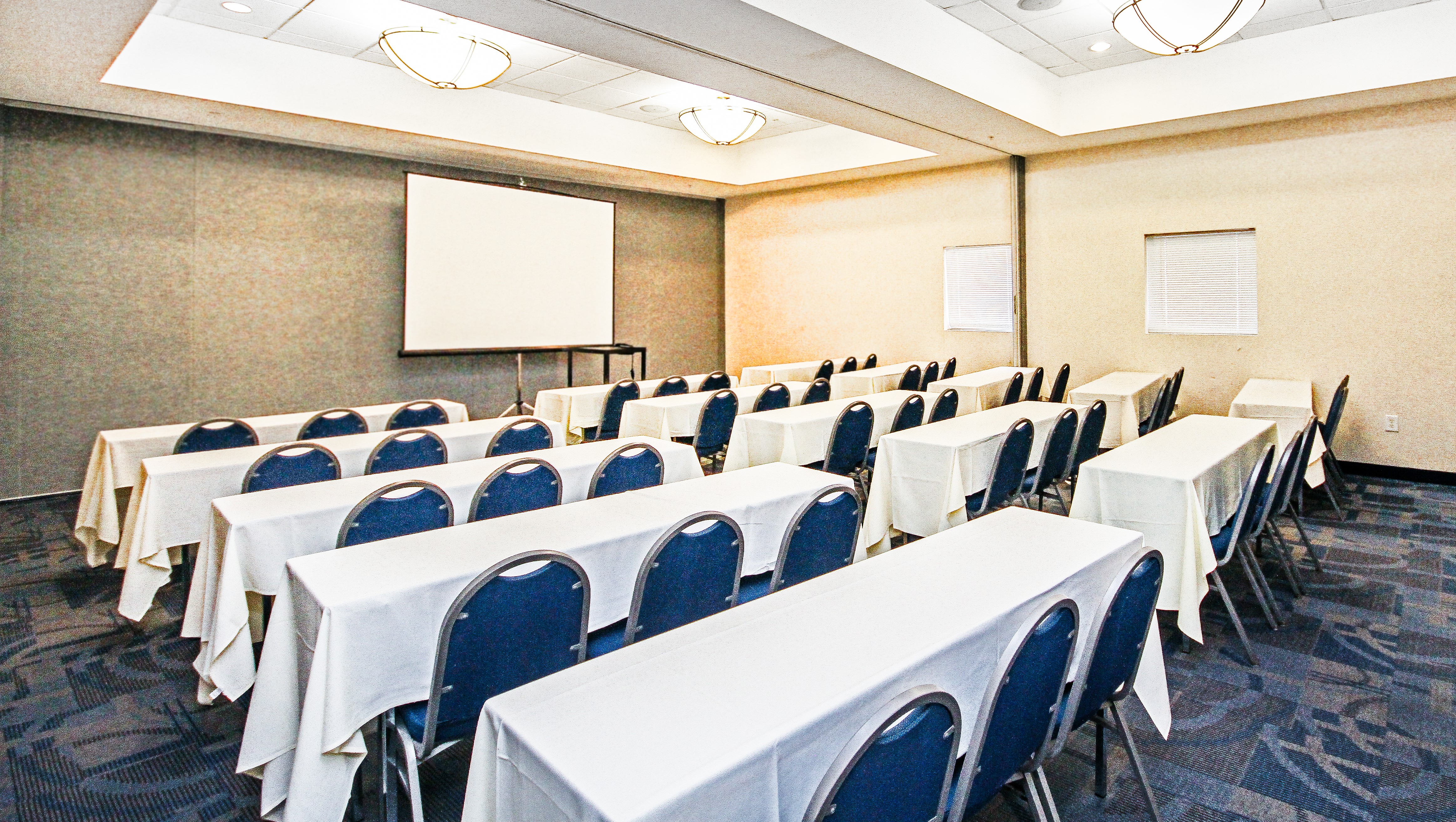 Tables and chairs facing a projector screen in a conference room.