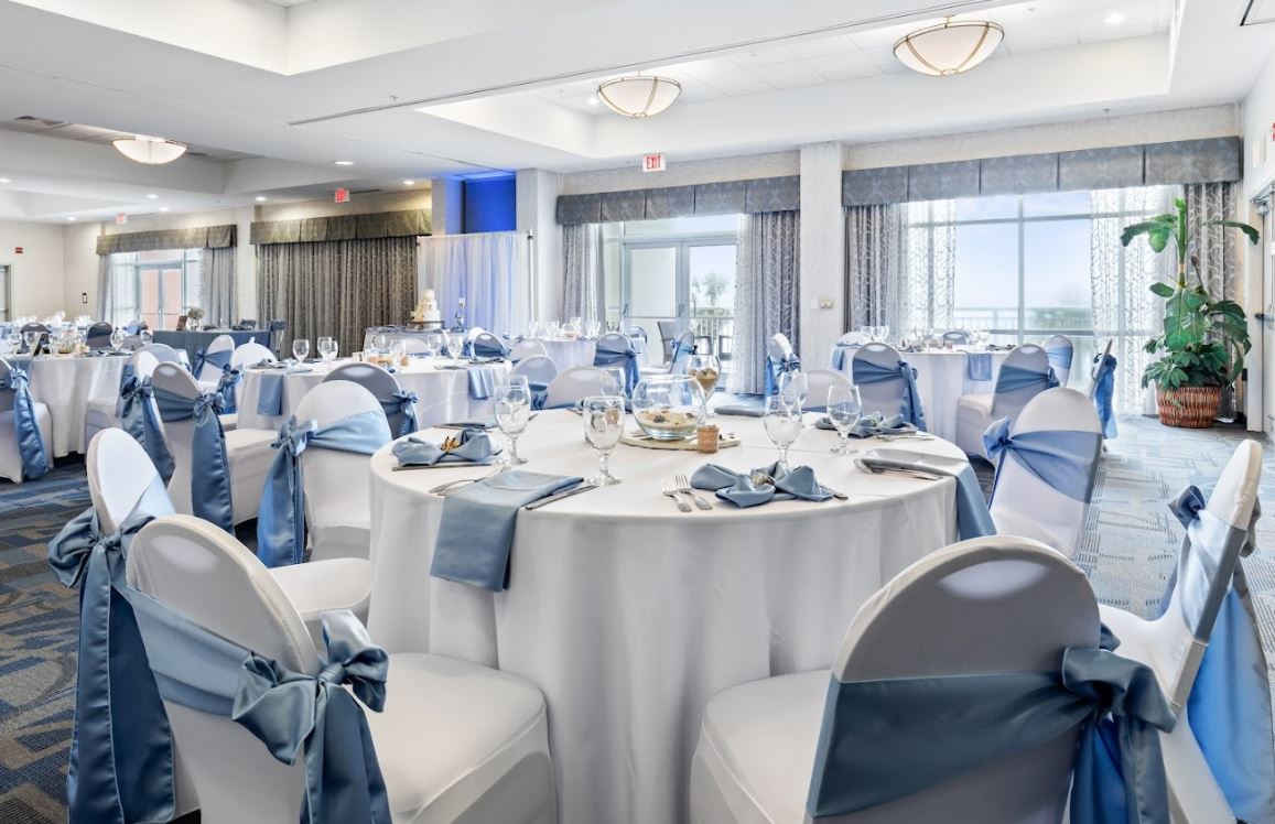 Tables and chairs draped in white wedding cloth and blue satin napkins in an indoor wedding venue at Bay Watch Resort.