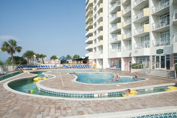 Children playing in a lazy river style outdoor pool at a resort with multiple story units.