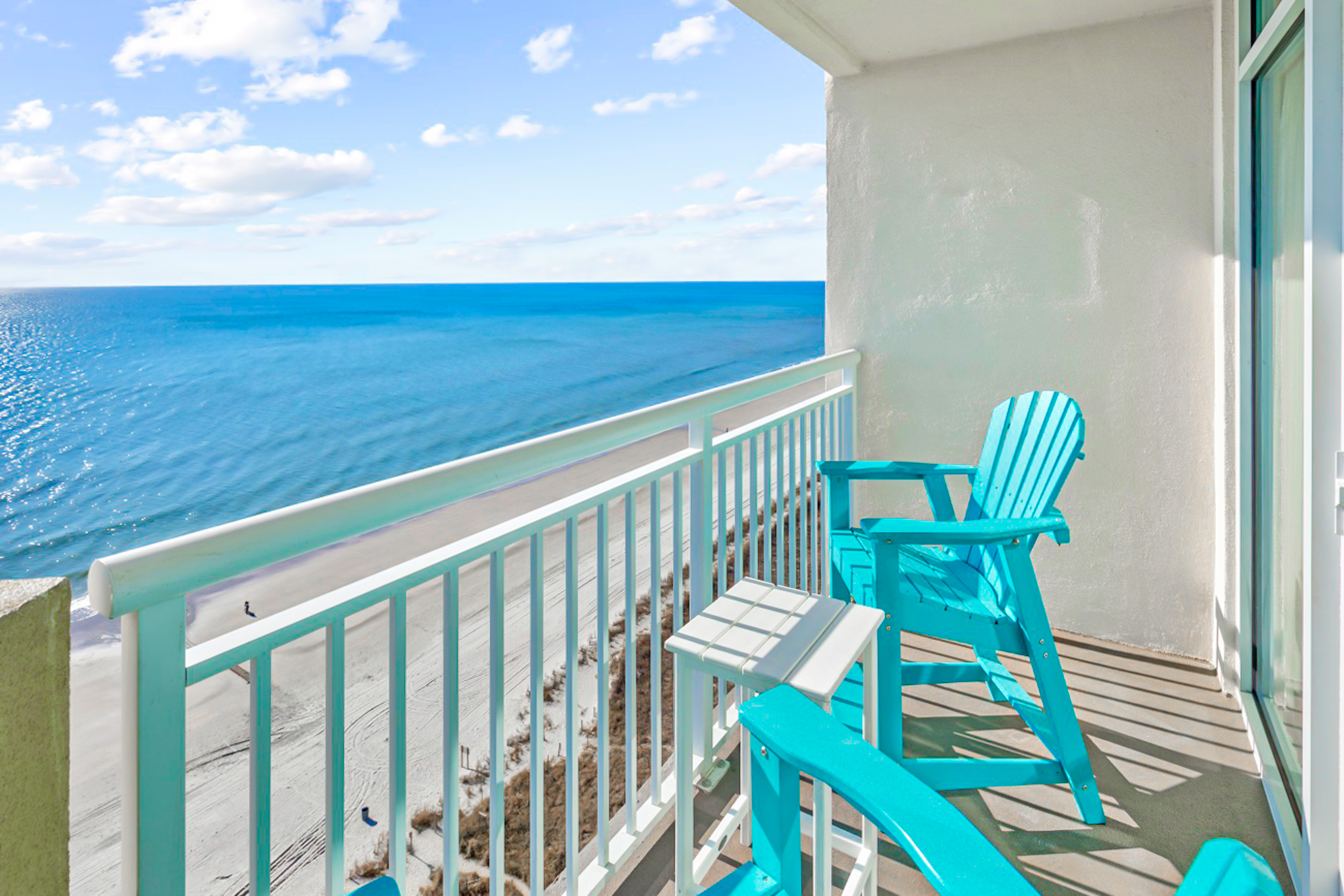 Aqua blue colored chairs on a balcony from a condo with a view of the ocean.