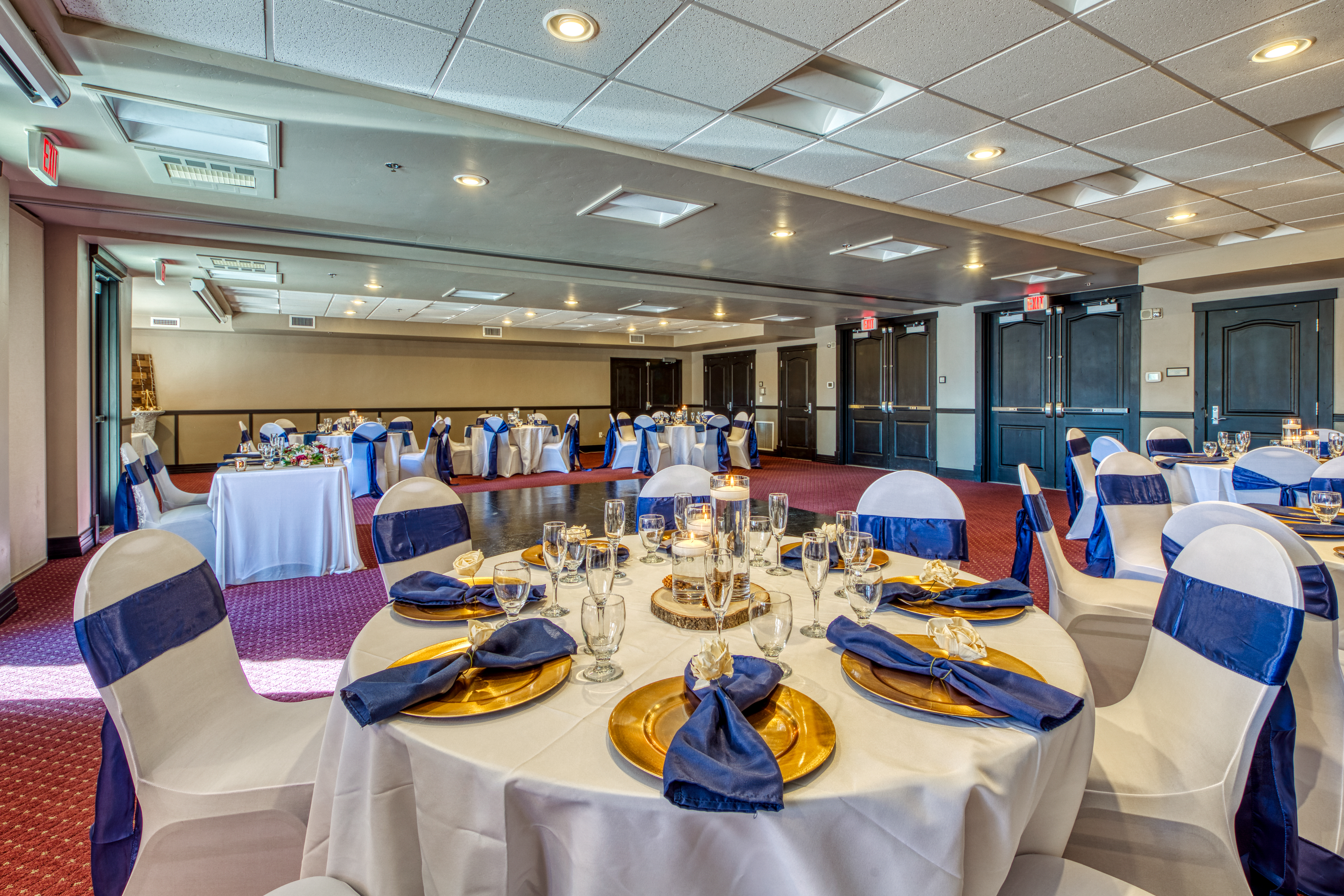 Indoor wedding venue with white linen tables, gold plates, silverware wrapped with blue cloth in Breckenridge, CO.