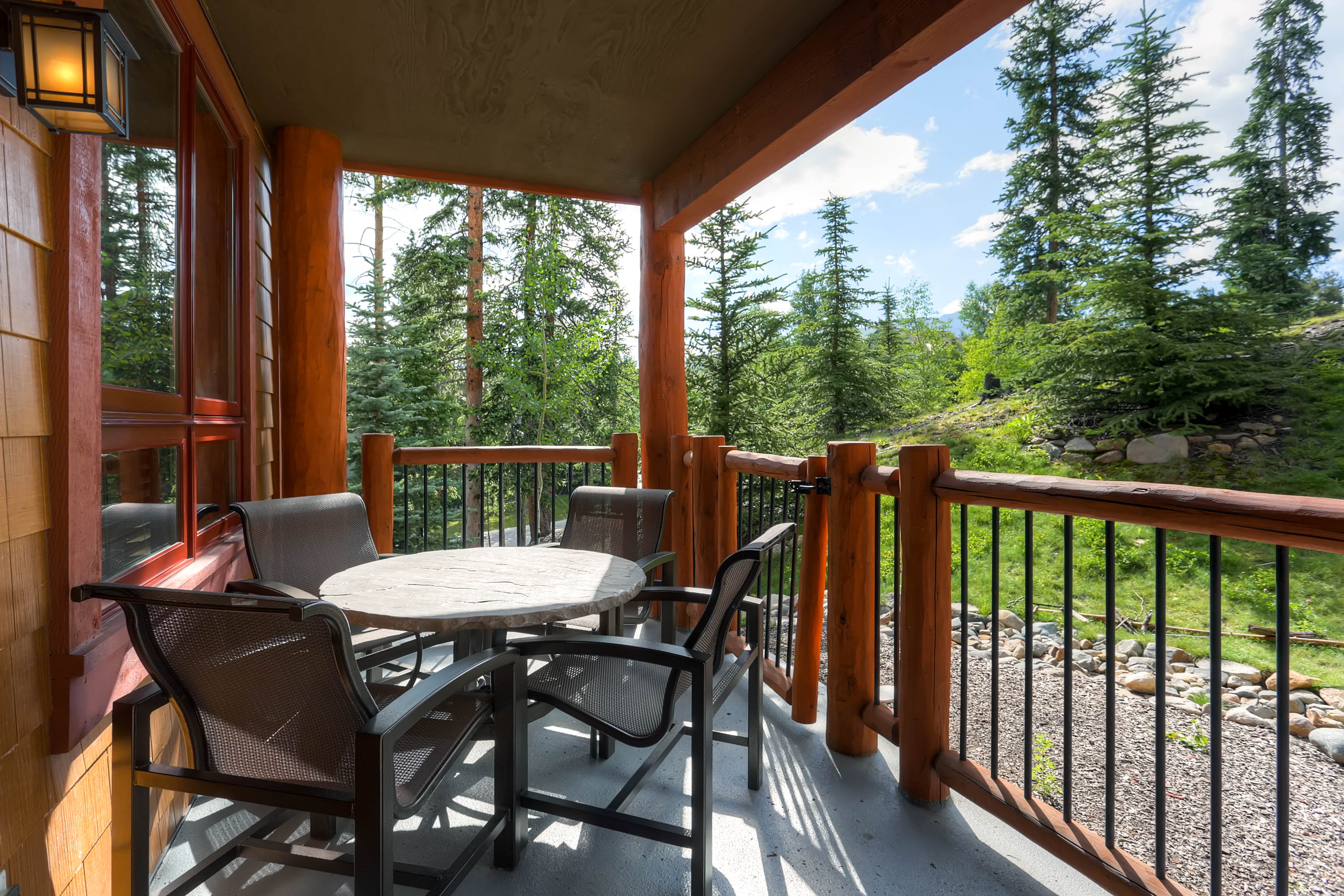 Outdoor balcony with a table and chairs facing a forest view.