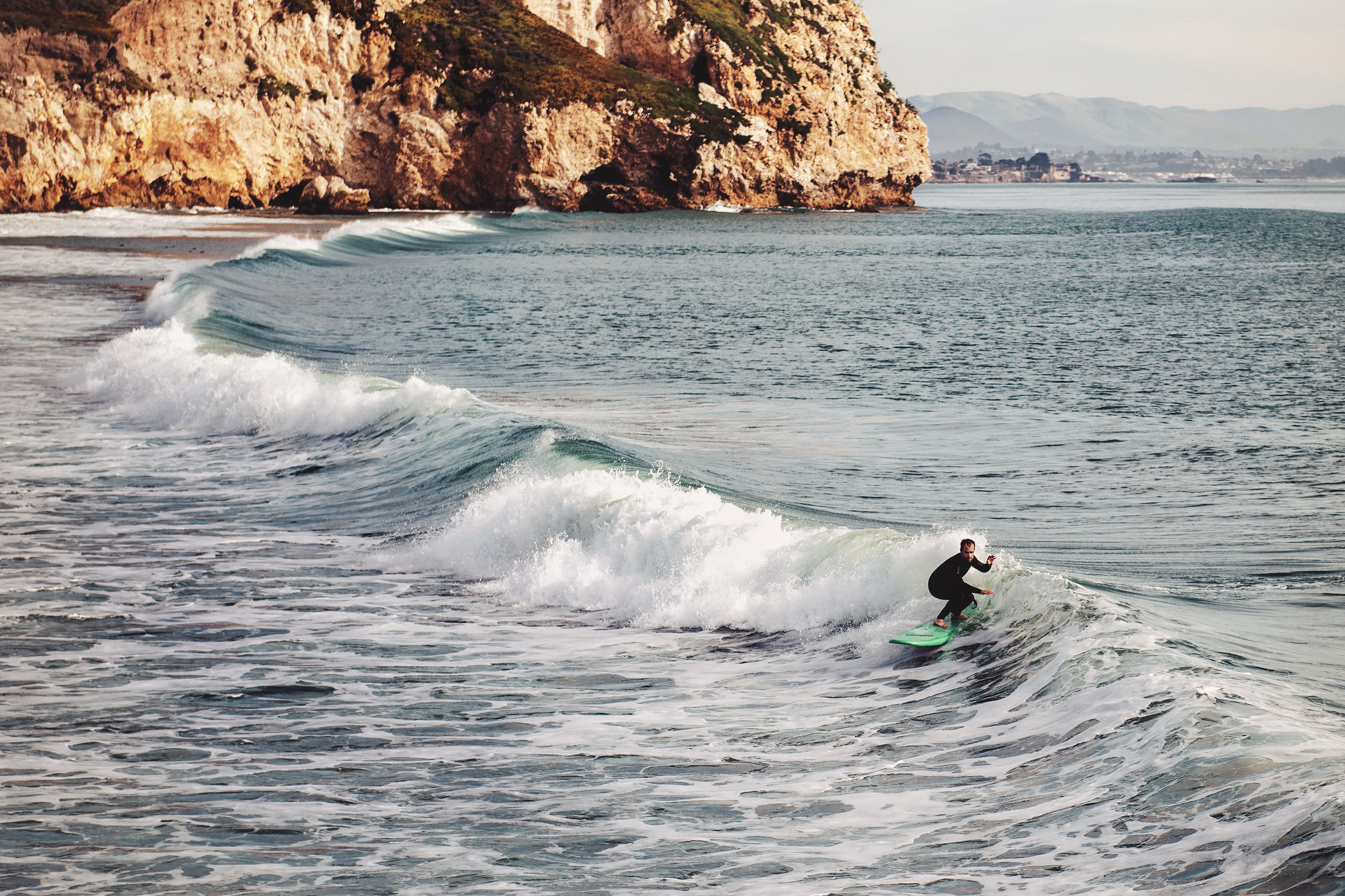 A single surfer surfing along the California coast