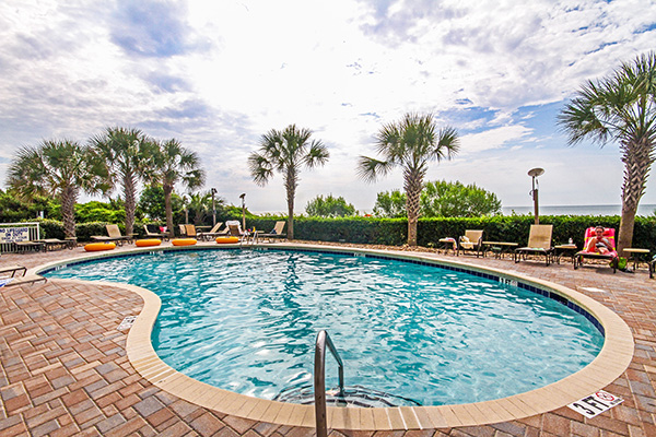 Outdoor pool with brick style ground surrounded by pool chairs and palm trees in Myrtle Beach, SC.
